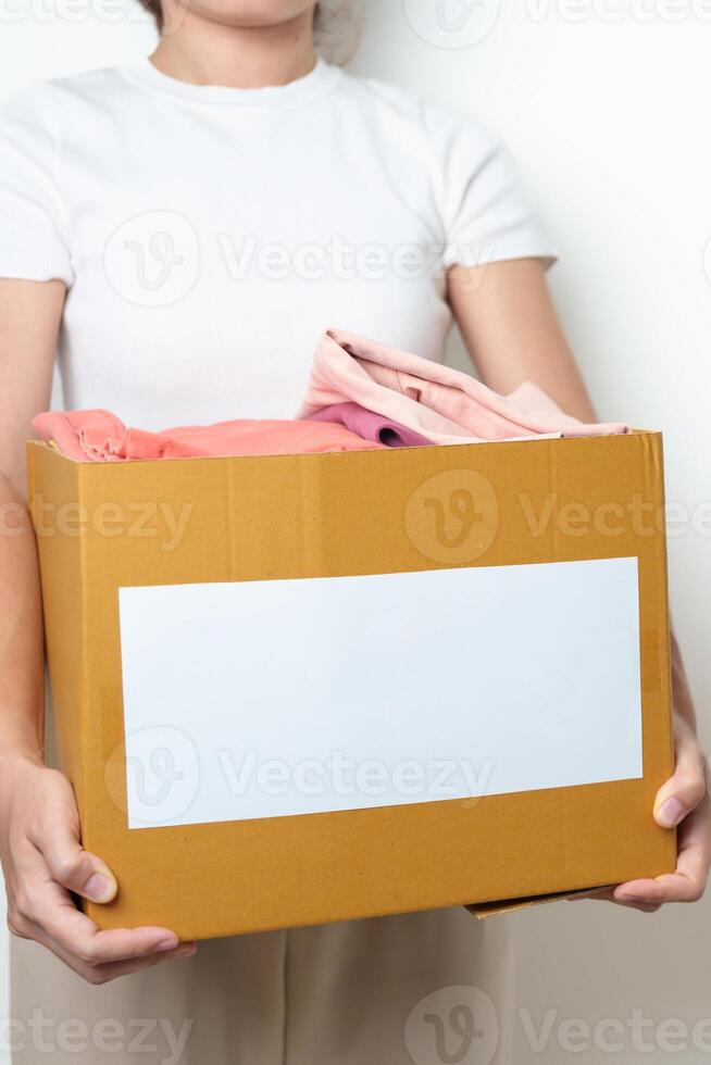Donation, Charity, Volunteer, Giving, Delivery and Home Moving Concept. Hand holding Clothes into cardboard box at home for support and help poor, refugee and homeless people. Copy space for text photo