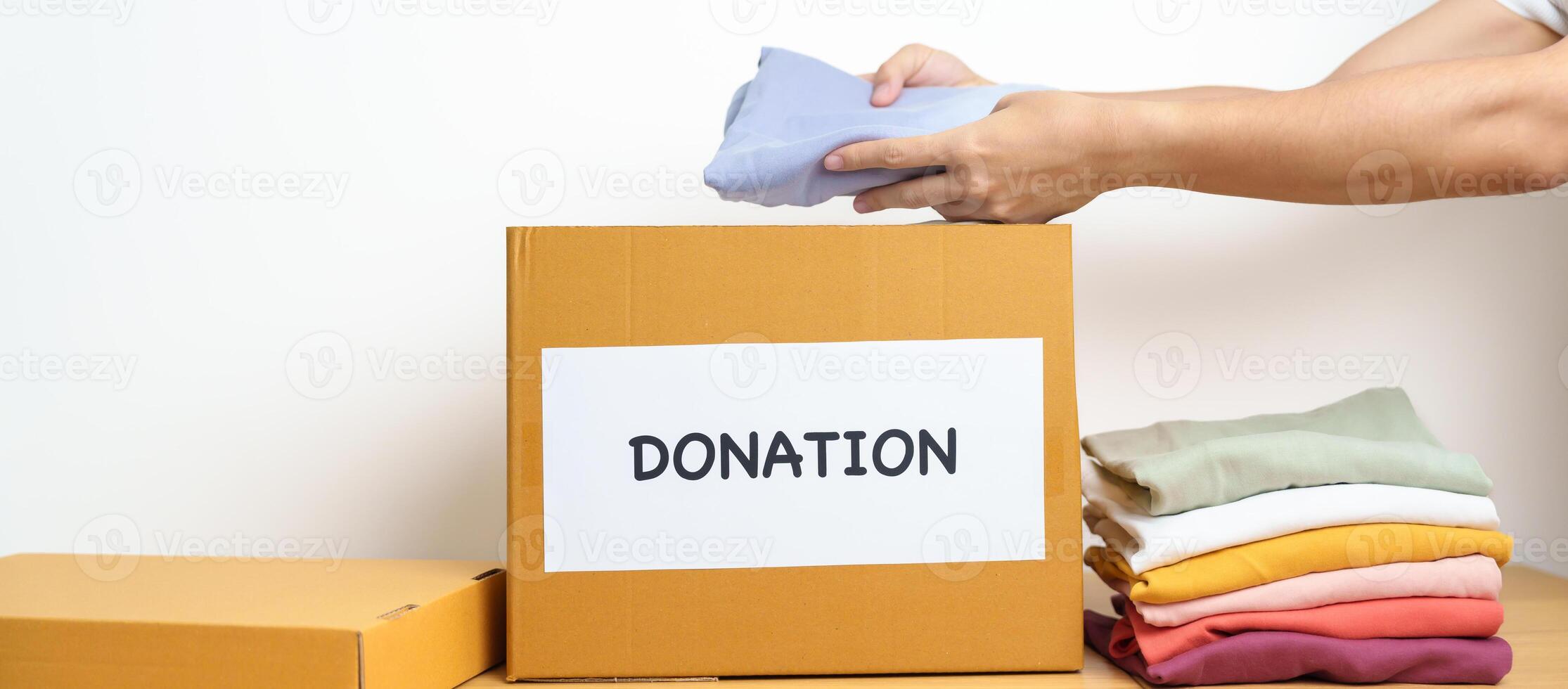 Donation, Charity, Volunteer, Giving and Delivery Concept. Hand holding Clothes into Donation box at home or office for support and help poor, refugee and homeless people. Copy space for text photo