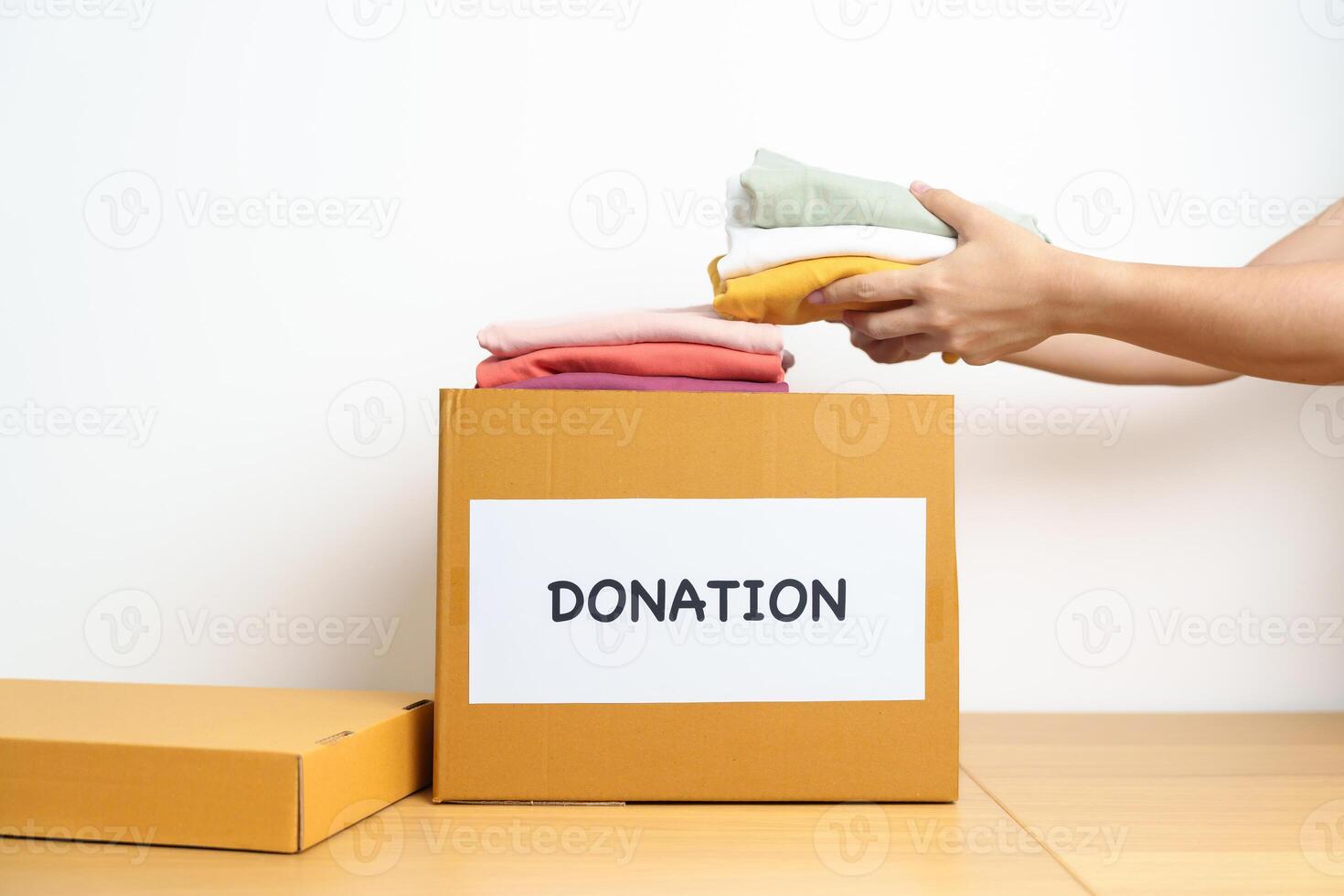 Donation, Charity, Volunteer, Giving and Delivery Concept. Hand holding Clothes into Donation box at home or office for support and help poor, refugee and homeless people. Copy space for text photo
