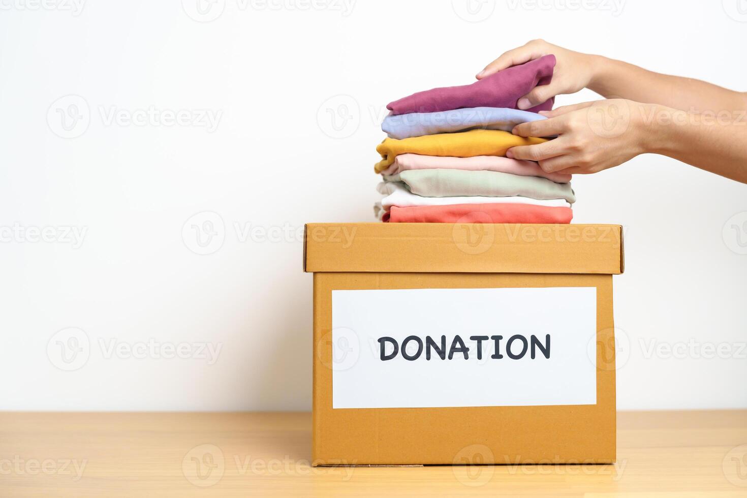 Donation, Charity, Volunteer, Giving and Delivery Concept. Hand holding Clothes into Donation box at home or office for support and help poor, refugee and homeless people. Copy space for text photo