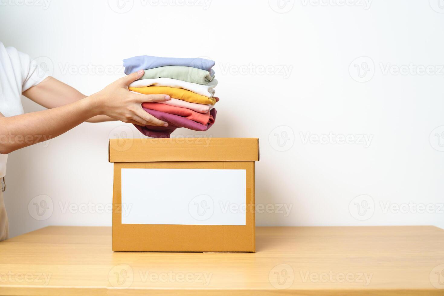 Donation, Charity, Volunteer, Giving, Delivery and Home Moving Concept. Hand holding Clothes into cardboard box at home for support and help poor, refugee and homeless people. Copy space for text photo