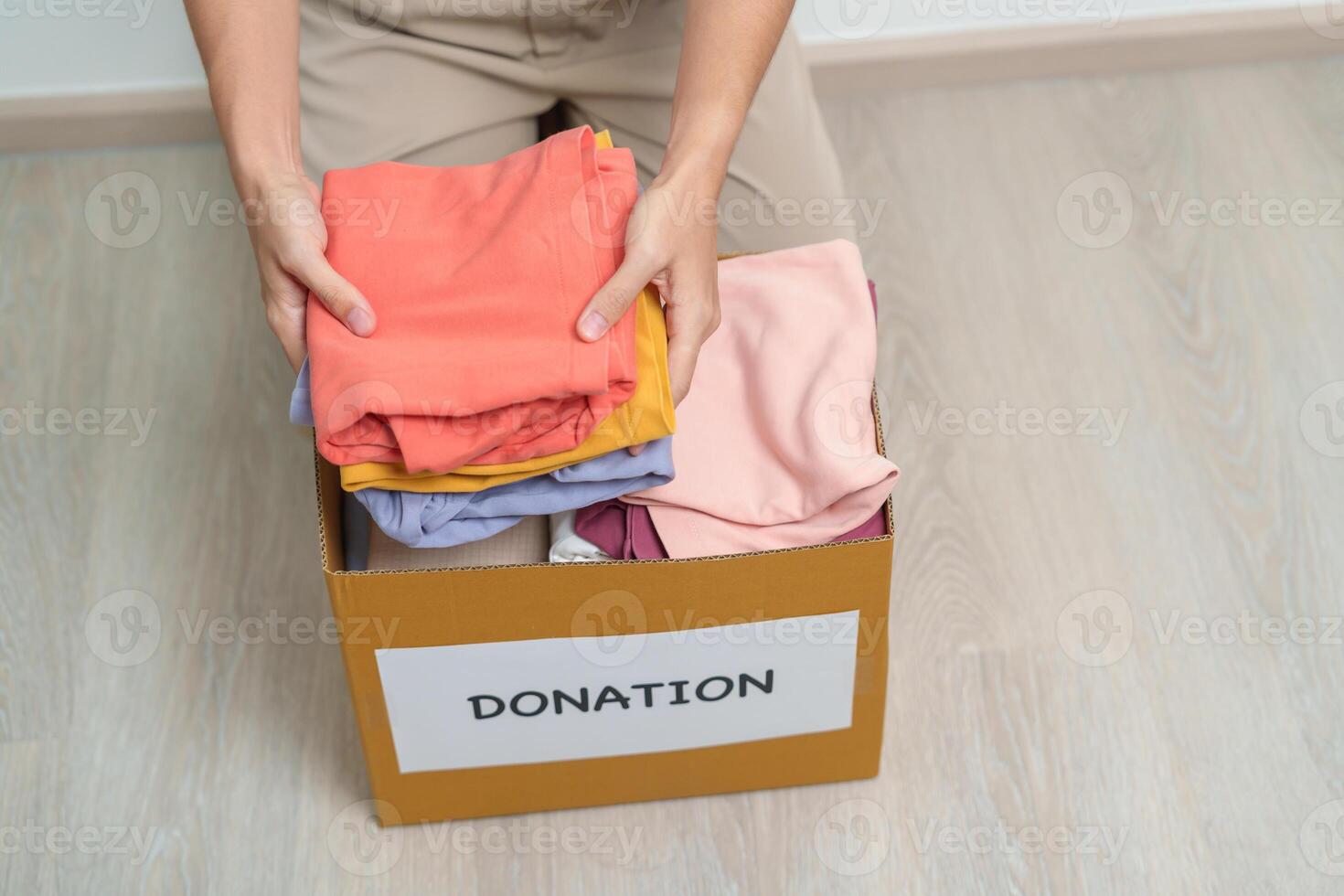 Donation, Charity, Volunteer, Giving and Delivery Concept. Hand holding Clothes into Donation box at home or office for support and help poor, refugee and homeless people. Copy space for text photo