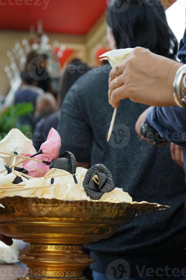 Defocused hand of people picks up the paper flower from the tray during funeral in Buddhism temple with blurred crowded people in background photo