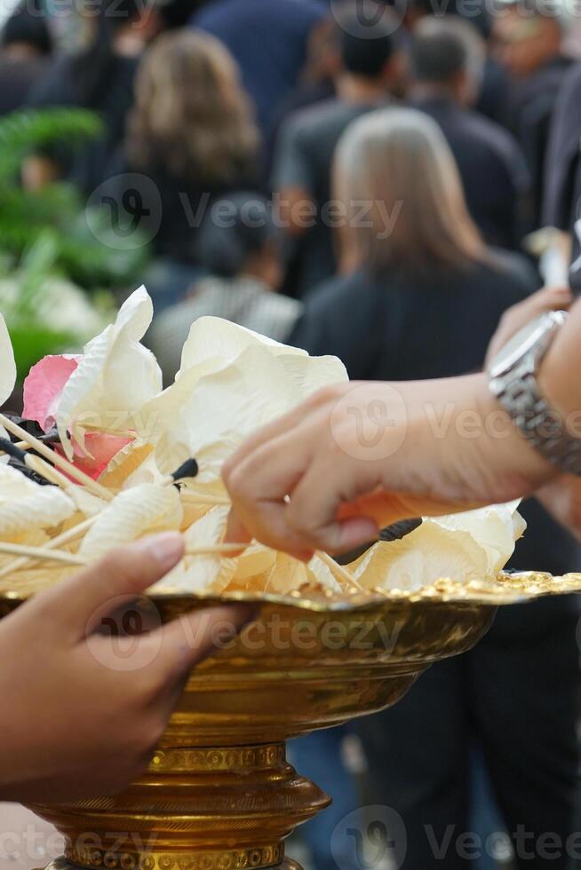 Defocused hand of people picks up the paper flower from the tray during funeral in Buddhism temple with blurred crowded people in background photo