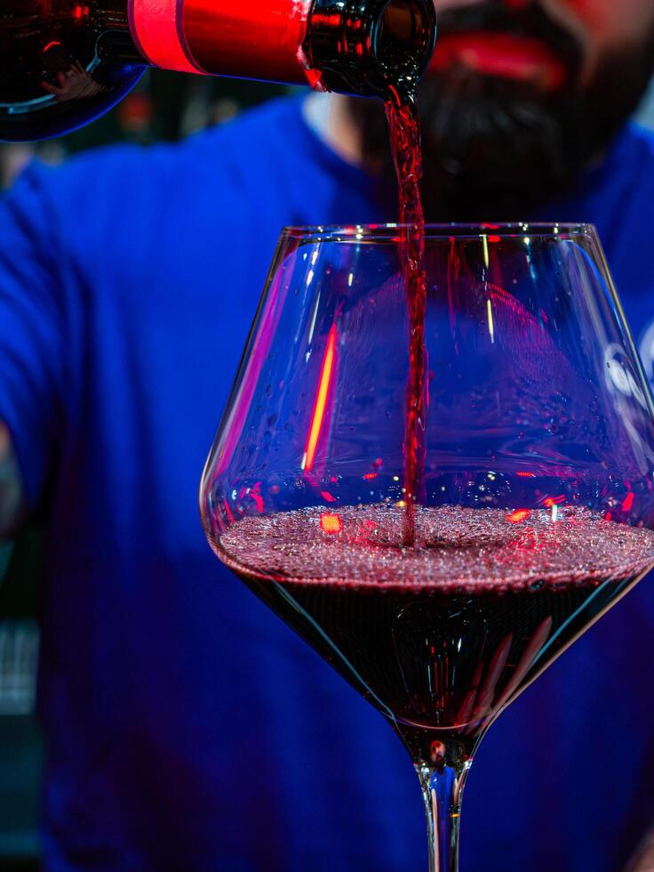 vertical close-up shot of a glass where the bartender pours red wine photo