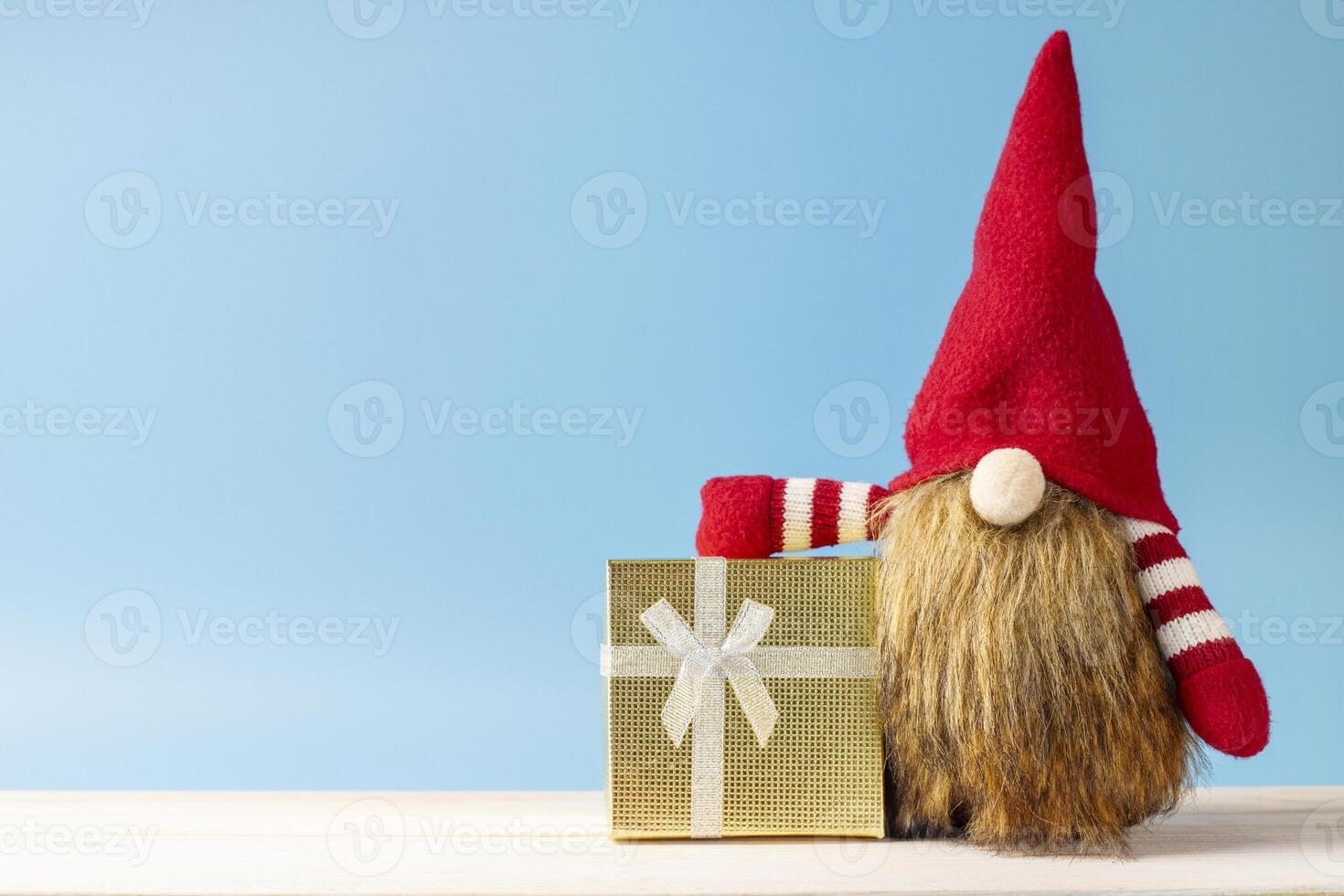 Cute Christmas gnome with golden gift box on blue background. Space for text photo