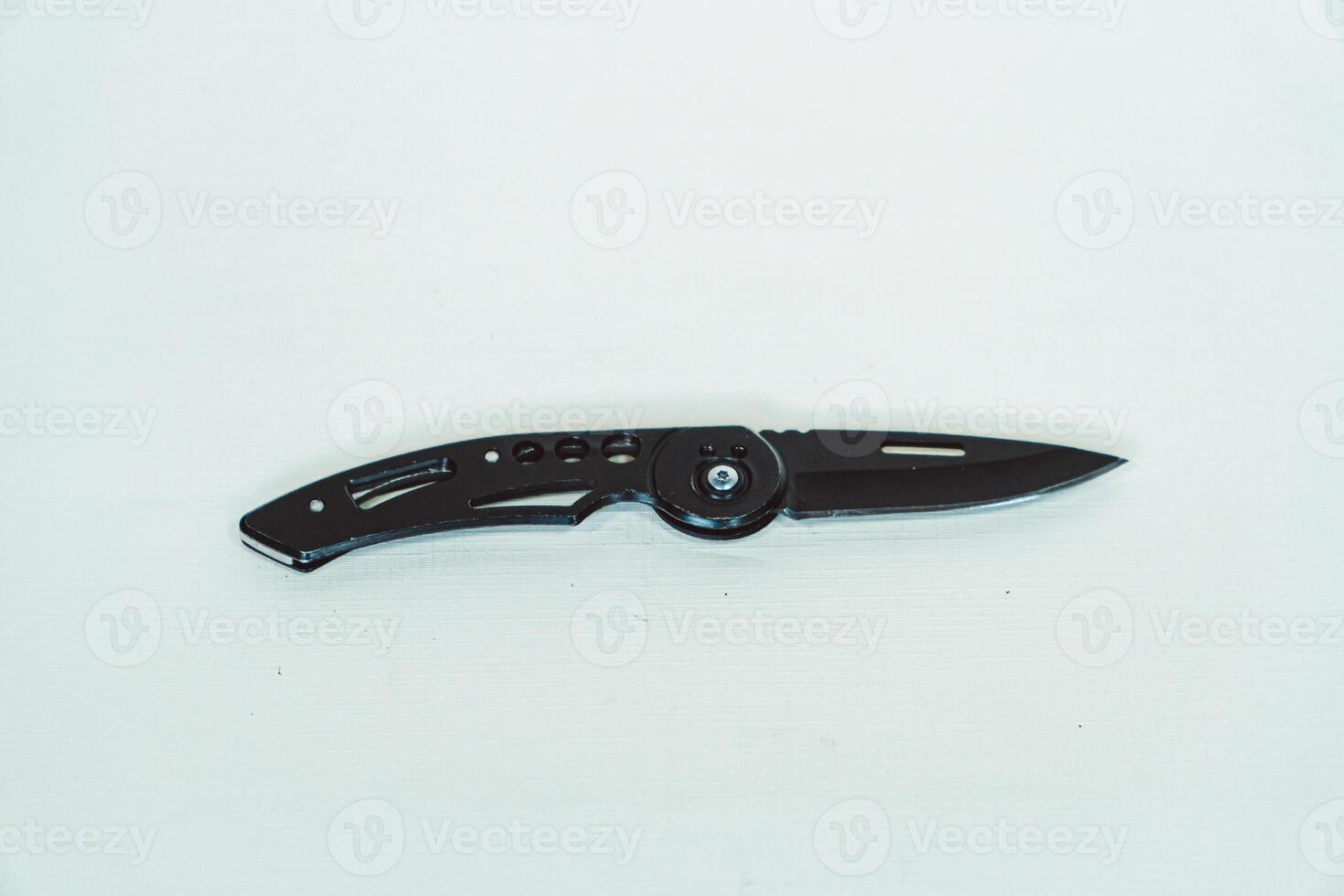 Mini size folding knife of solid black color partially opened isolated on white background. Close-up view of a black folding knife used for various outdoor or survival activities photo