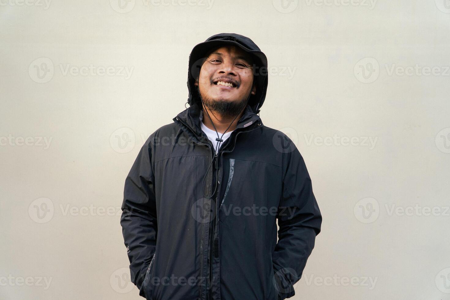 Portrait of Asian man wearing adventure clothes and doing various poses. Macho and smiling adult man wearing white shirt and jacket with hood isolated on beige background photo