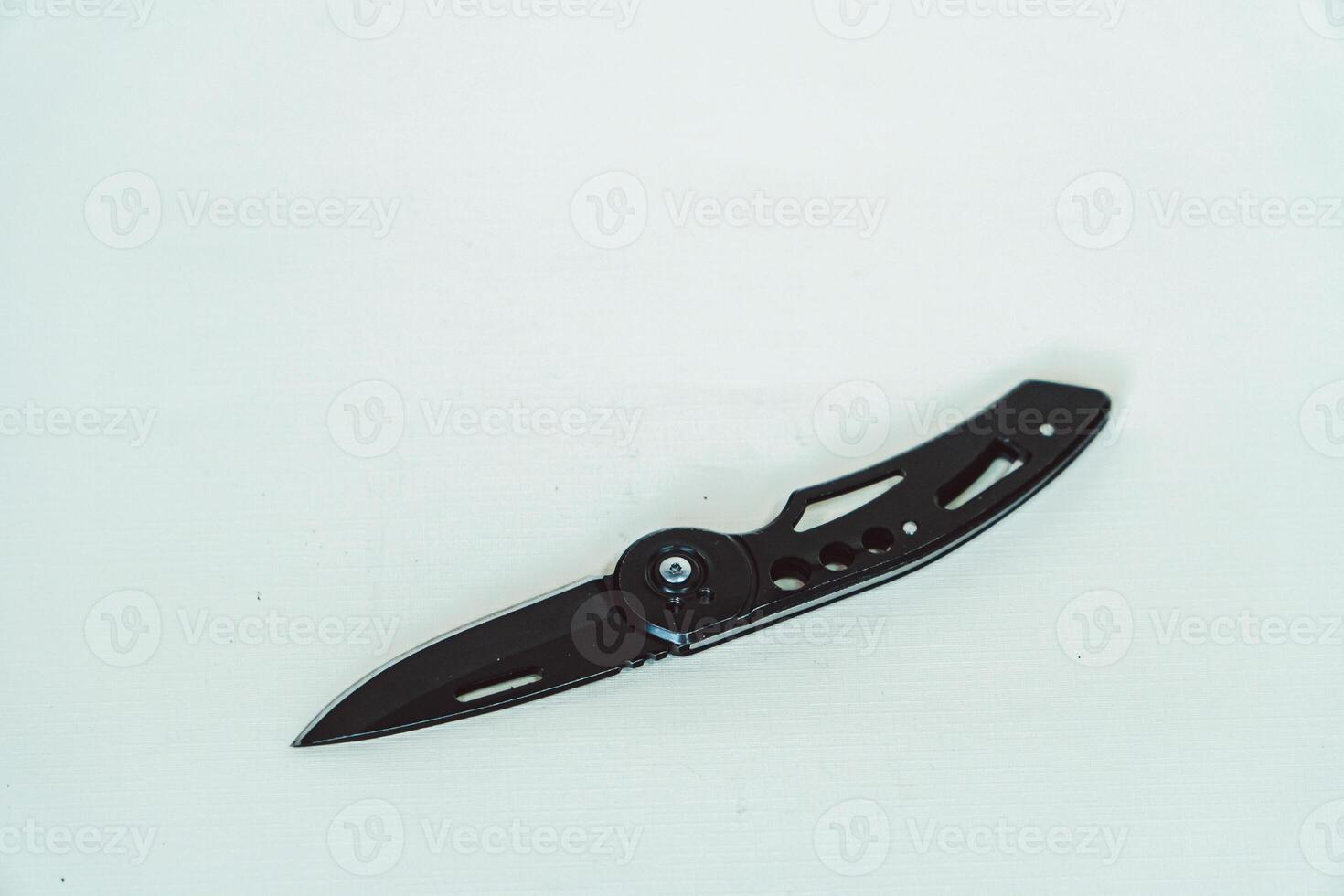Mini size folding knife of solid black color partially opened isolated on white background. Close-up view of a black folding knife used for various outdoor or survival activities photo