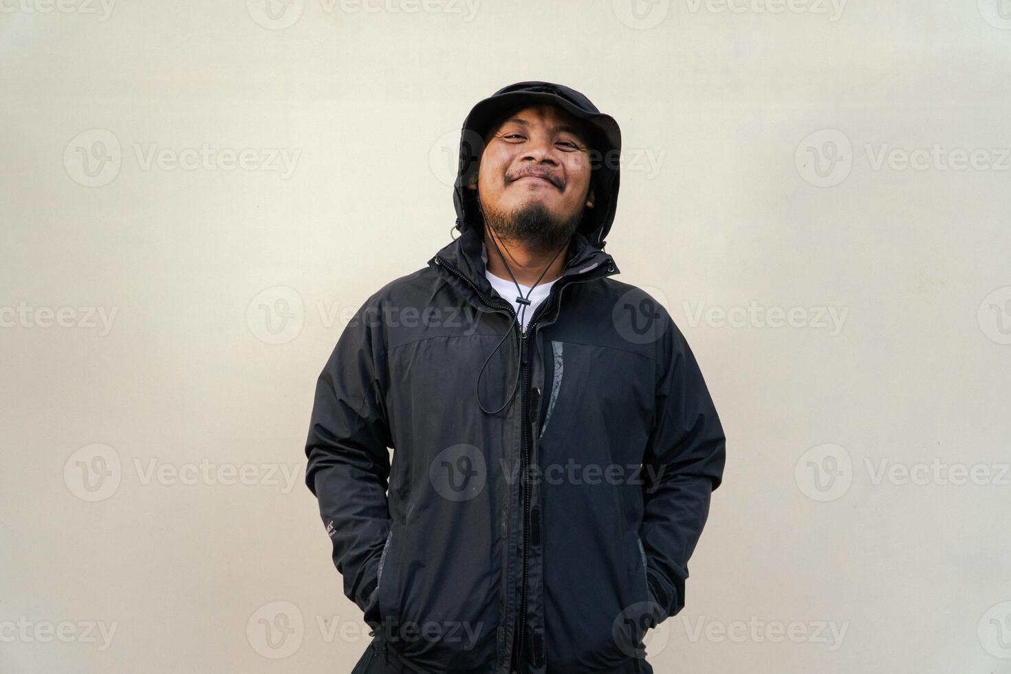 Portrait of Asian man wearing adventure clothes and doing various poses. Macho and smiling adult man wearing white shirt and jacket with hood isolated on beige background photo