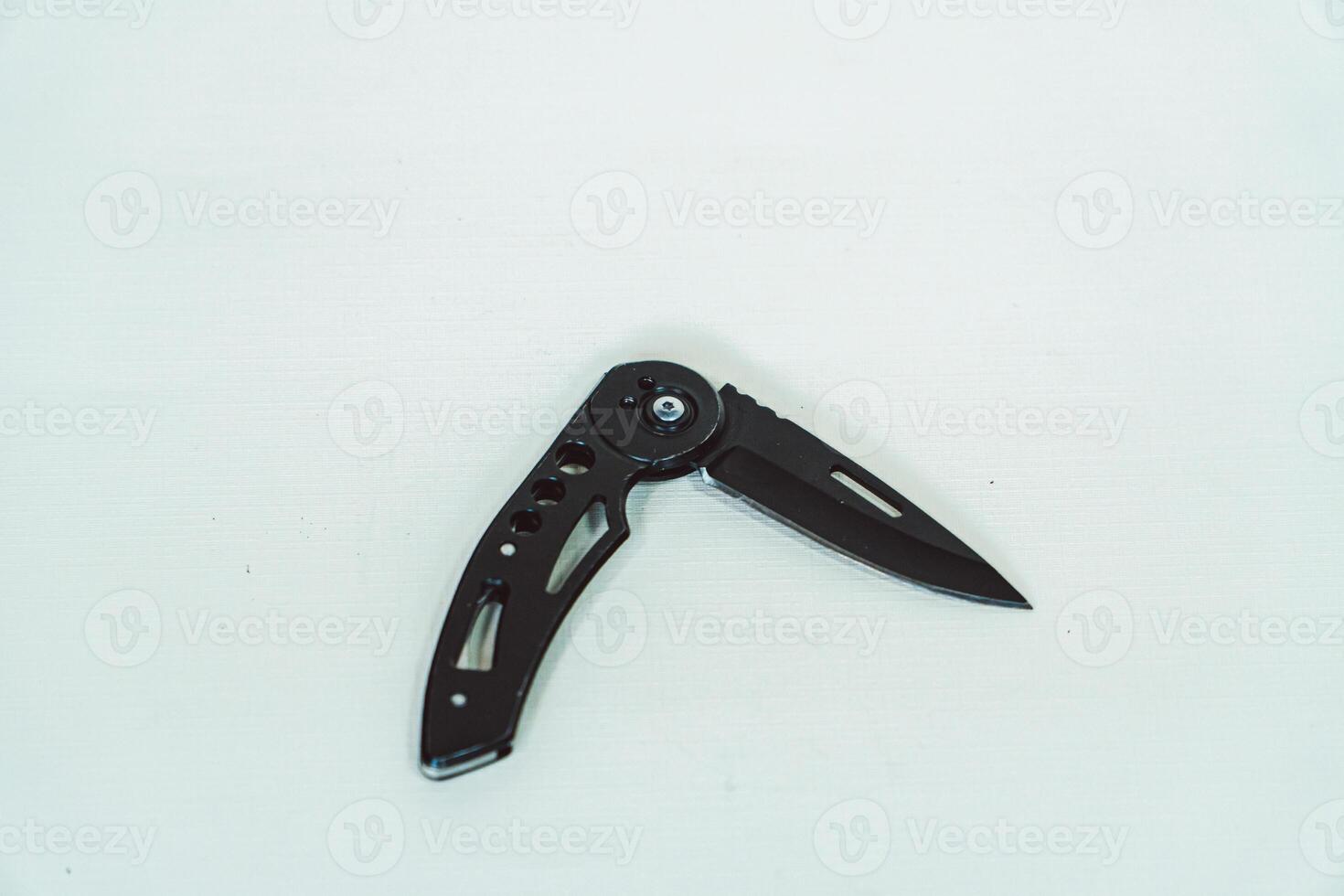 Mini size folding knife of solid black color partially opened isolated on white background. Close-up view of a black folding knife used for various outdoor or survival activities photo