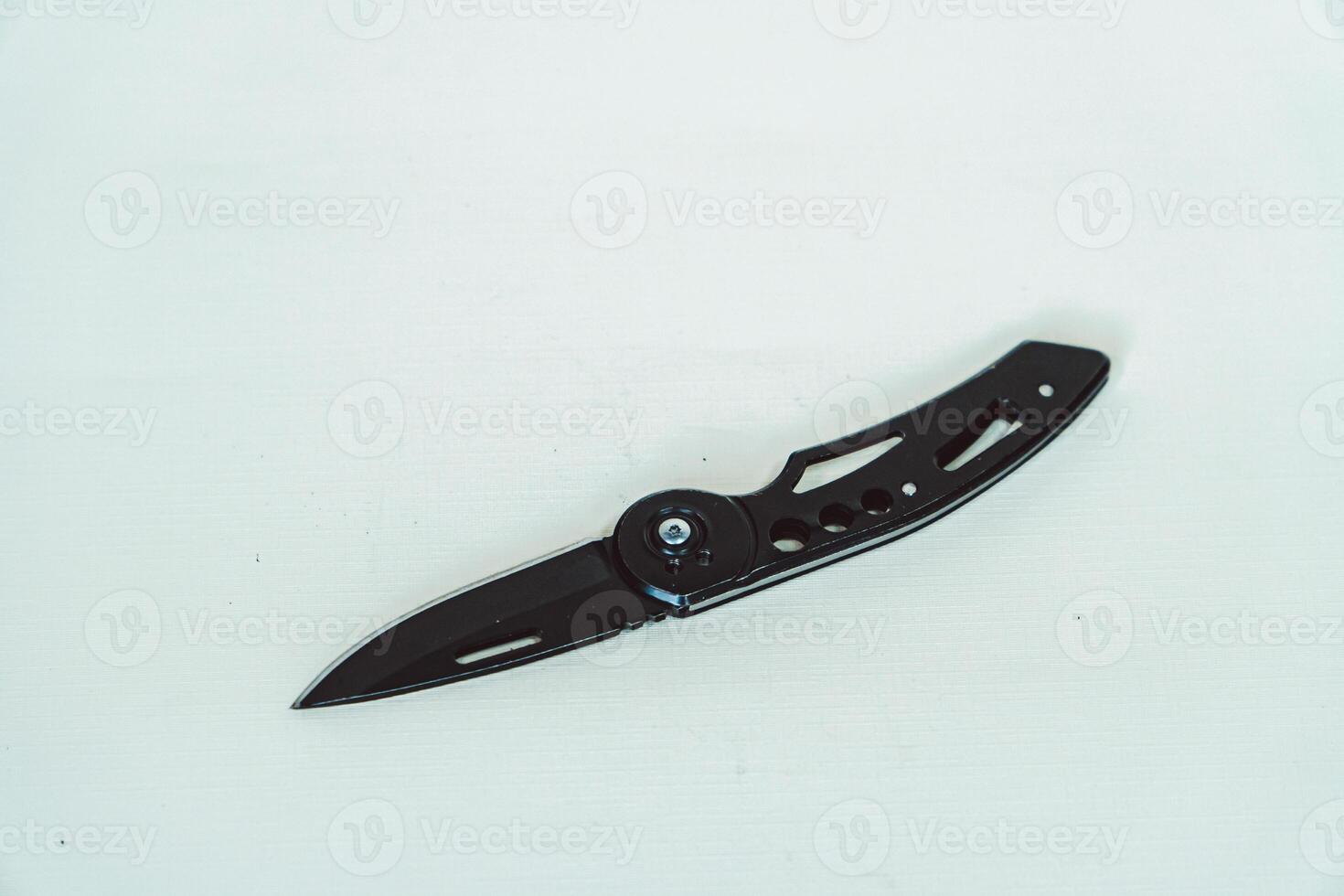 Mini size folding knife of solid black color partially opened isolated on white background. Close-up view of a black folding knife used for various outdoor or survival activities photo