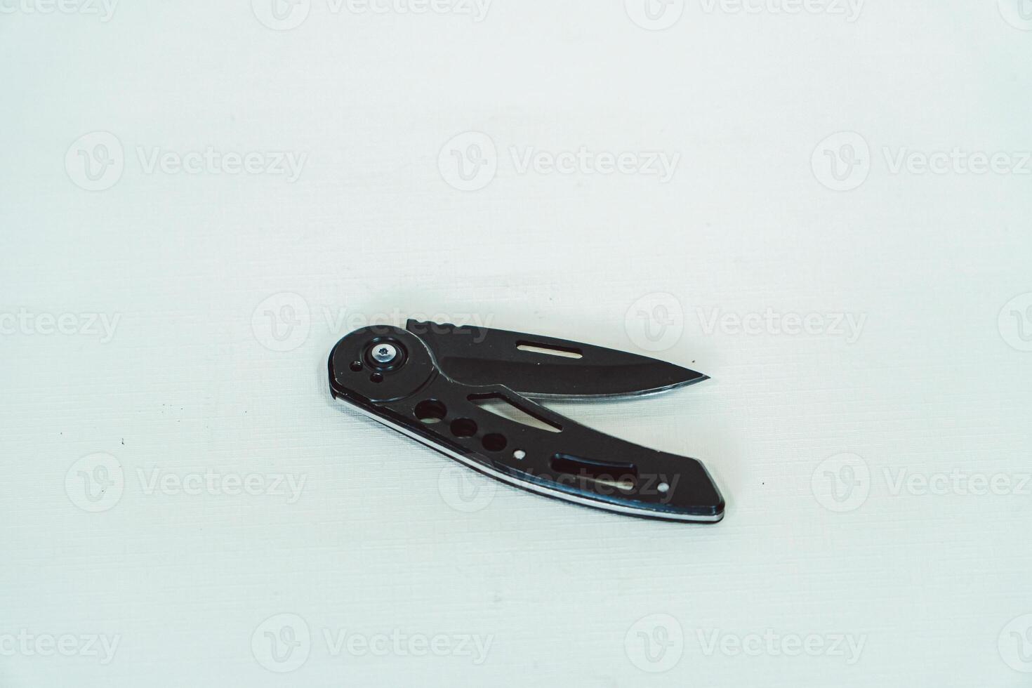 Mini size folding knife of solid black color partially opened isolated on white background. Close-up view of a black folding knife used for various outdoor or survival activities photo