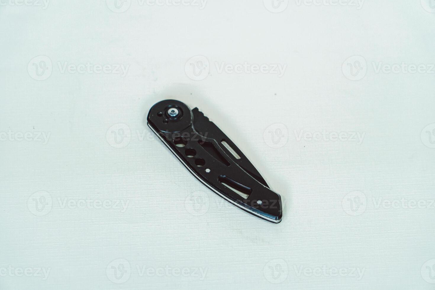 Mini size folding knife of solid black color partially opened isolated on white background. Close-up view of a black folding knife used for various outdoor or survival activities photo