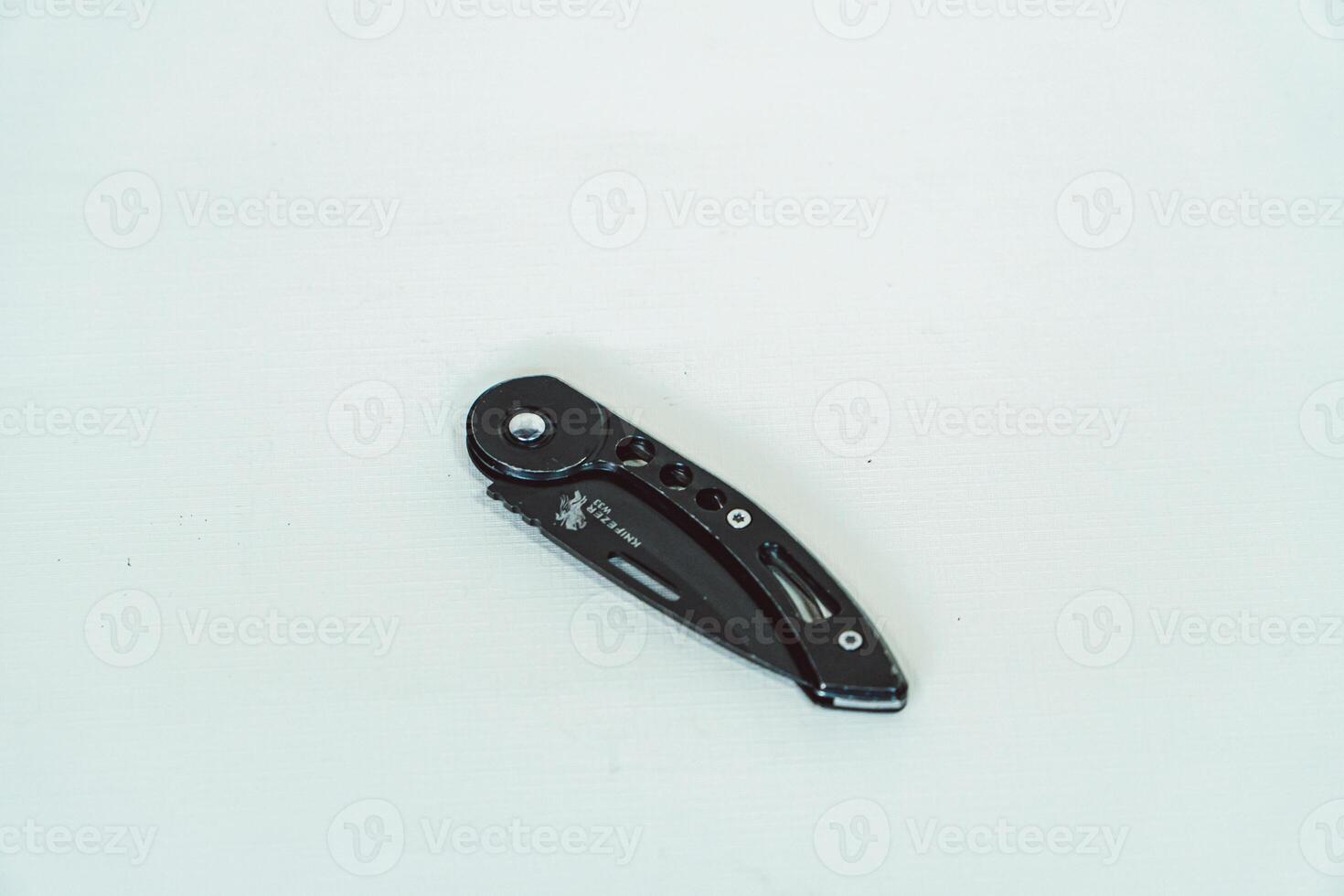 Mini size folding knife of solid black color partially opened isolated on white background. Close-up view of a black folding knife used for various outdoor or survival activities photo