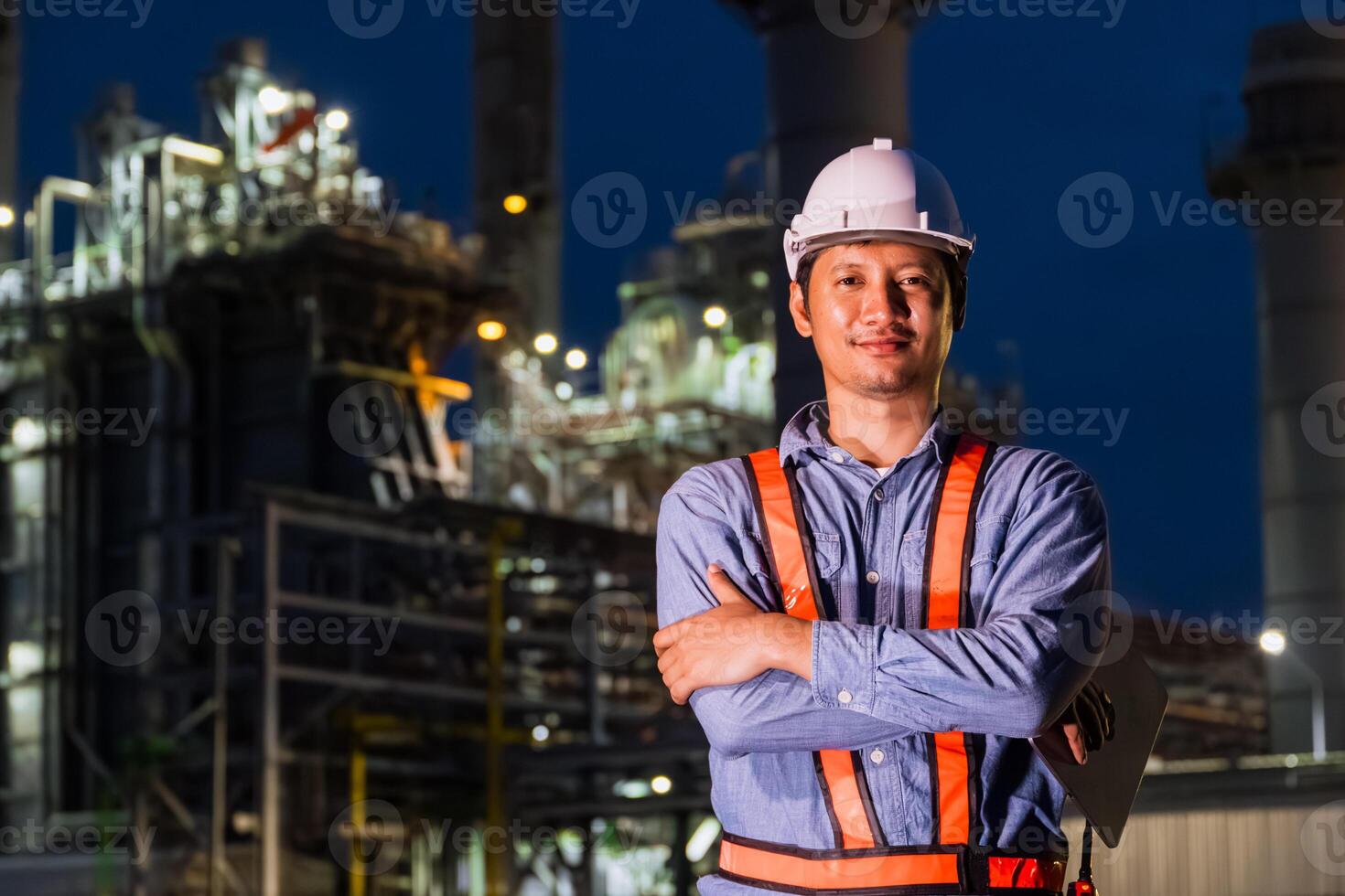 Engineer professional Asian male standing confident happy against Petroleum Refinery industry at Night. Oil and Gas Petrochemical Power plant business leader. photo