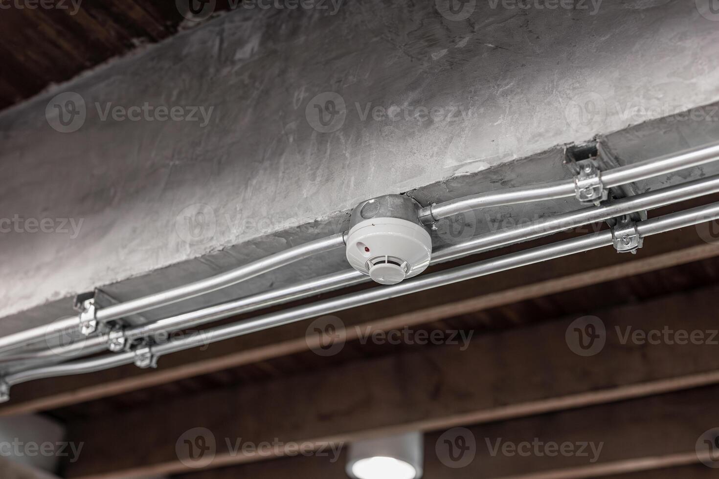 Smoke detector, fire alarm detector indoor home safety device with IMC metal pipeline at ceiling photo