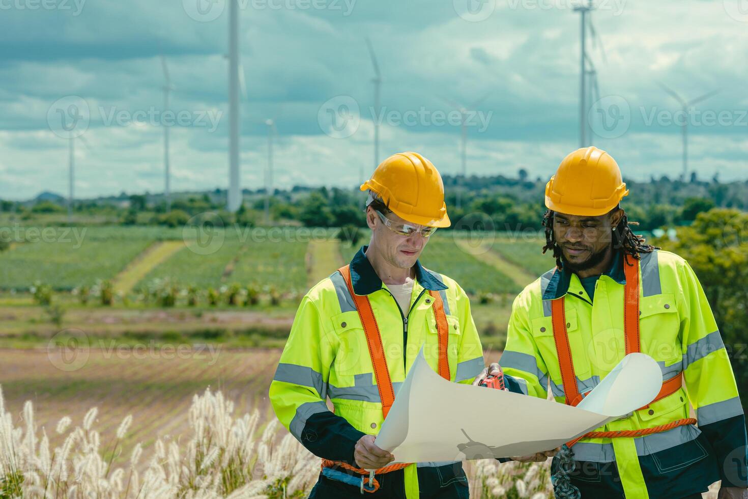 Engineer team mix black and white male workers with floor plan at Wind Turbines field working survey at wind electricity generator farm field outdoor. photo