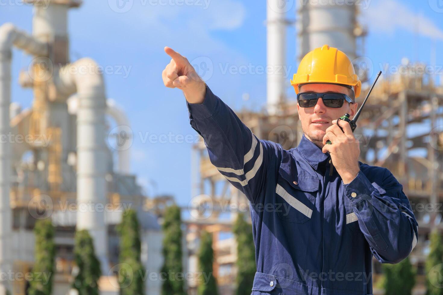 Petroleum industry engineer worker working outdoor. Refinery plant oil and gas service team control operate maintenance front of large complex gas pipe building with radio. photo