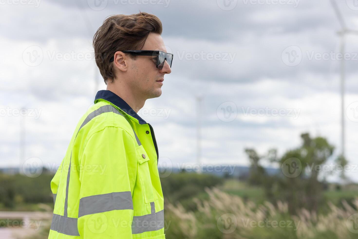 Smart young engineer technician male worker standing side view closeup at Wind Turbines clean power generator field background. photo