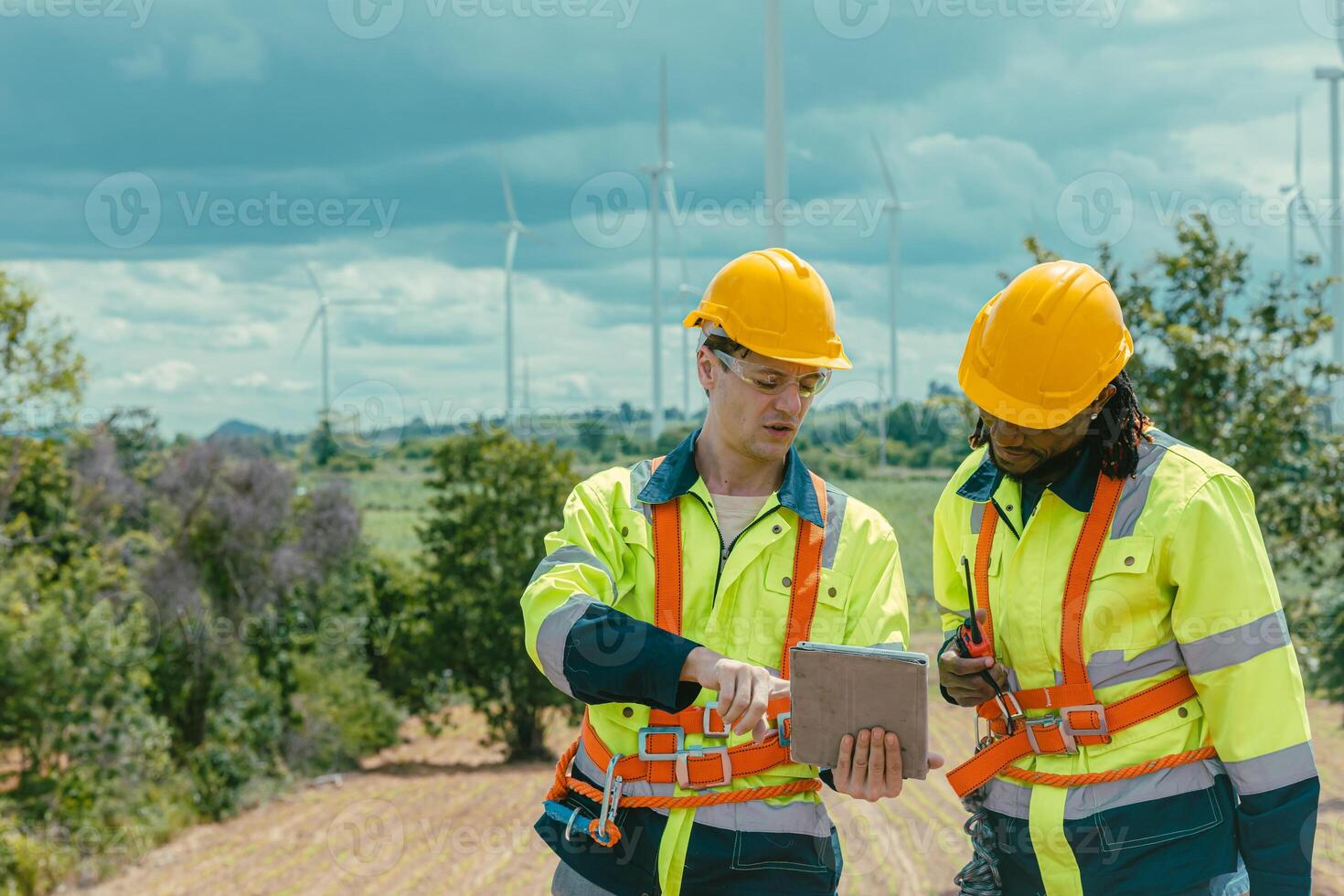 Engineer workers using tablet computer service monitor Wind Turbines status, working survey at wind electricity generator farm field outdoor. photo