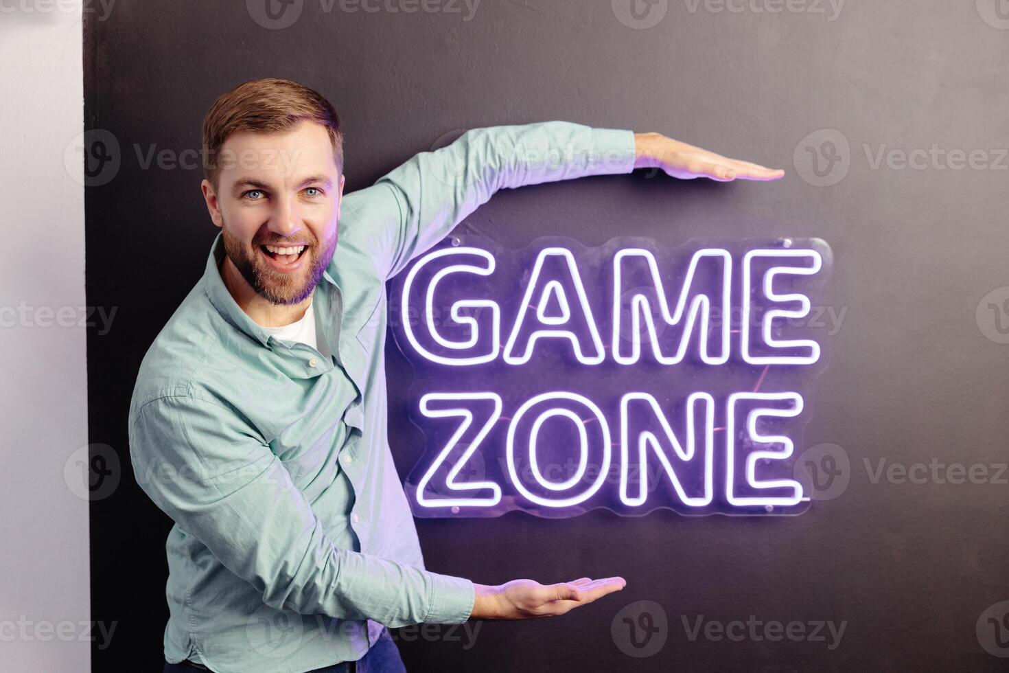 A young handsome man is standing near a wall with the inscription game zone. photo