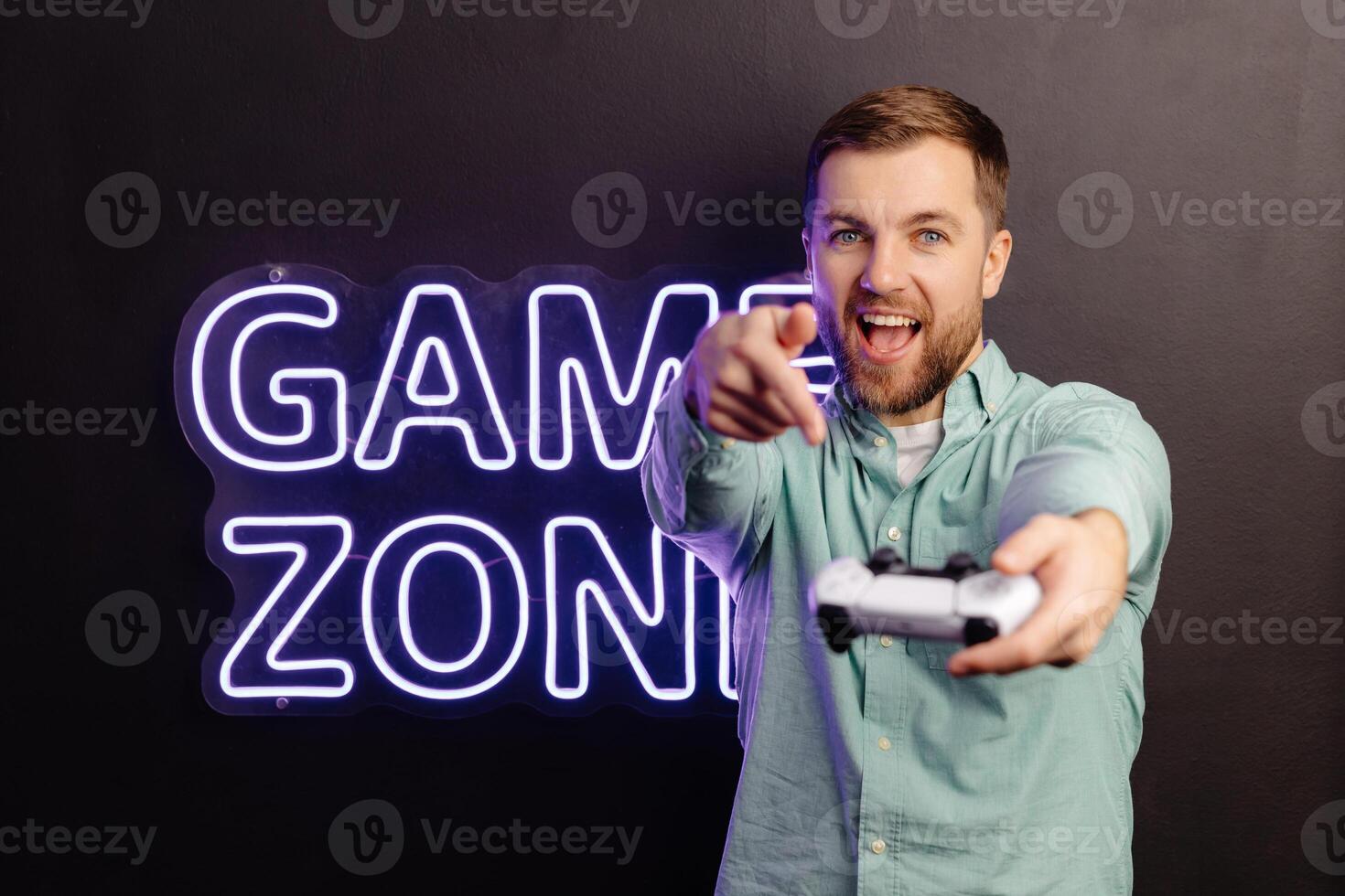 Young bearded man standing at the wall in the room and playing, holding wireless joystick, screaming, and winning intense game match photo