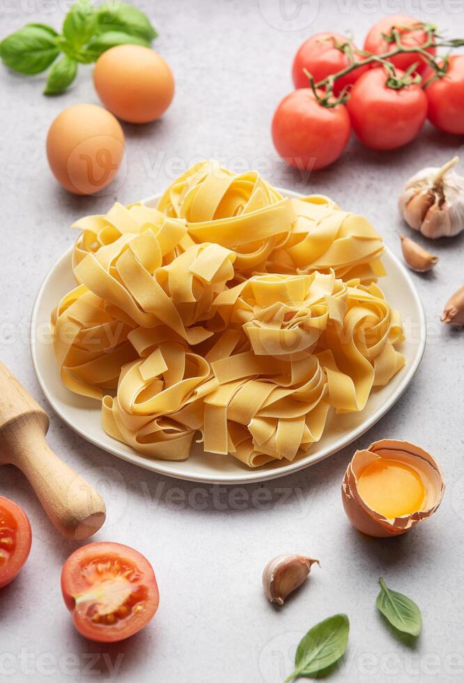 Uncooked pappardelle pasta with ingredients forming frame on table photo