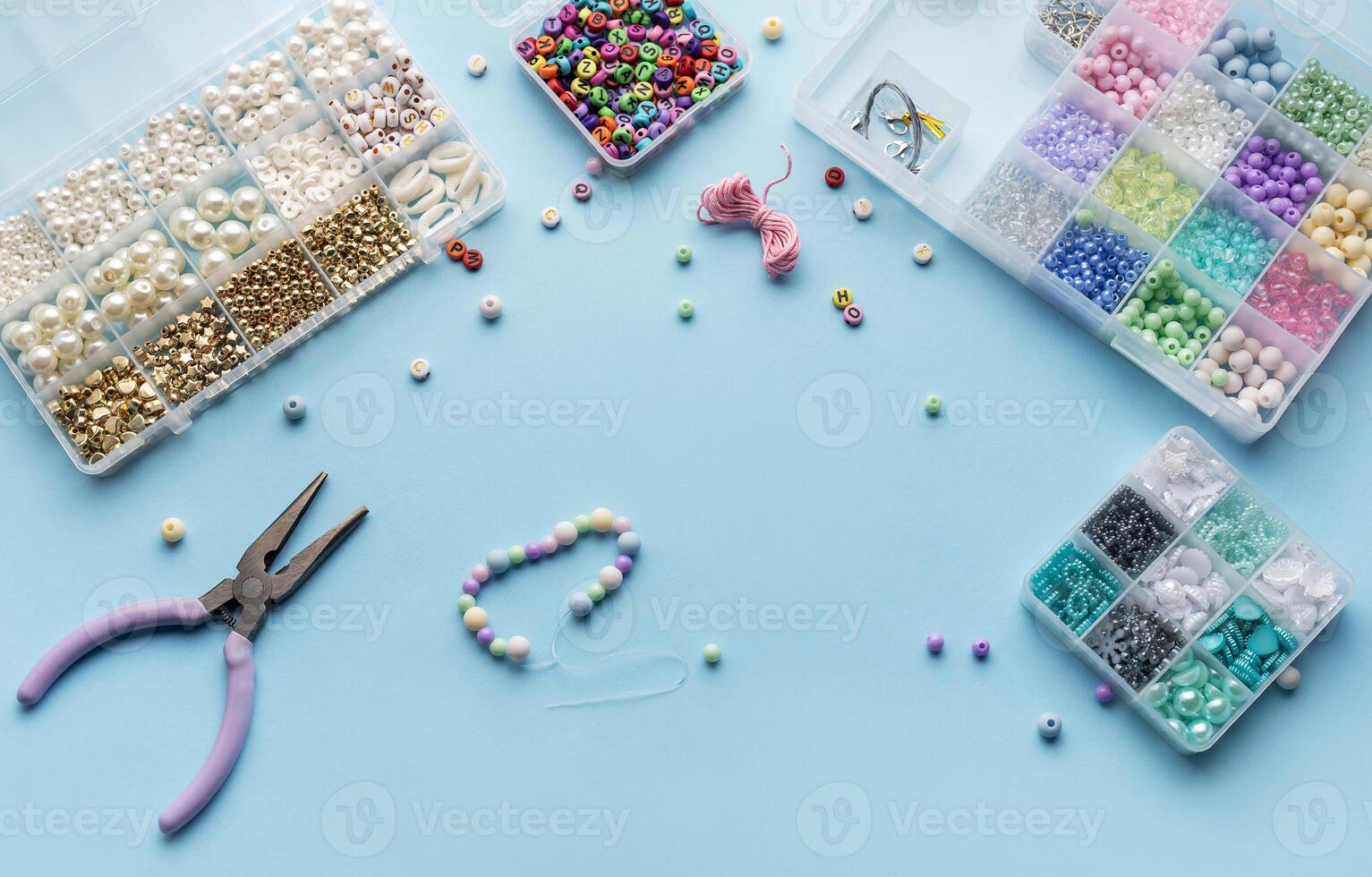 Crafting colorful beaded jewelry on a blue surface with tools and a variety of beads photo