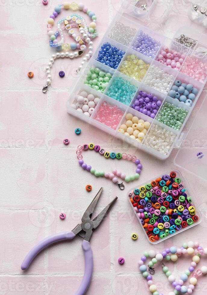 Colorful beads and pliers arranged on pink tile for jewelry making photo