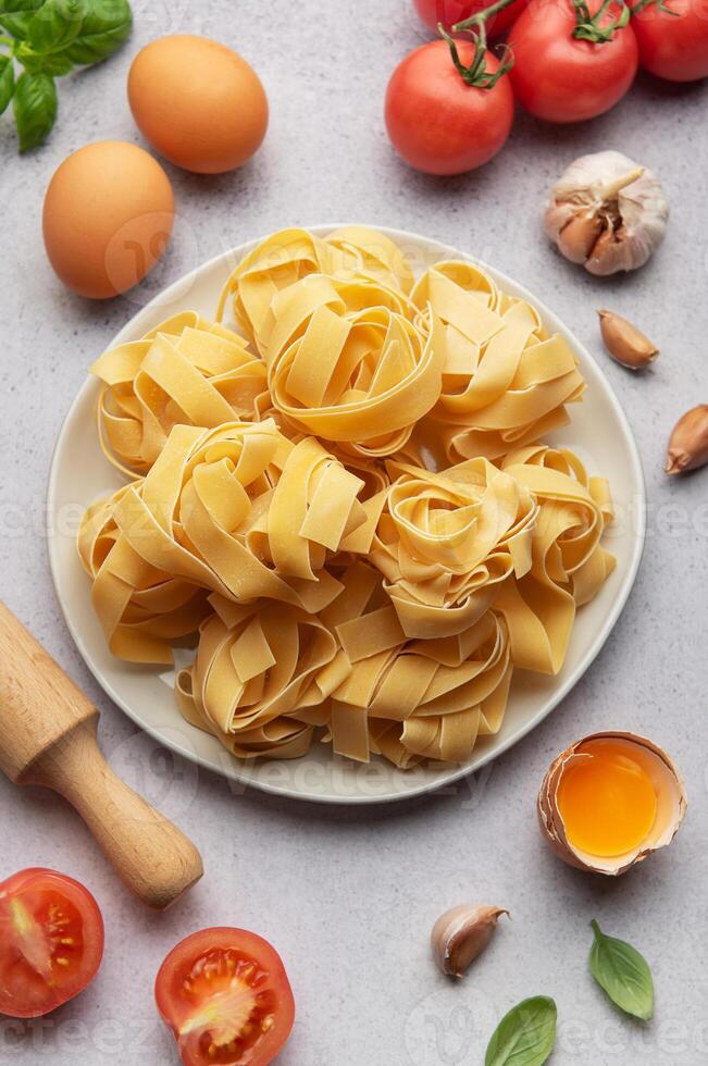 Uncooked pappardelle pasta with ingredients forming frame on table photo