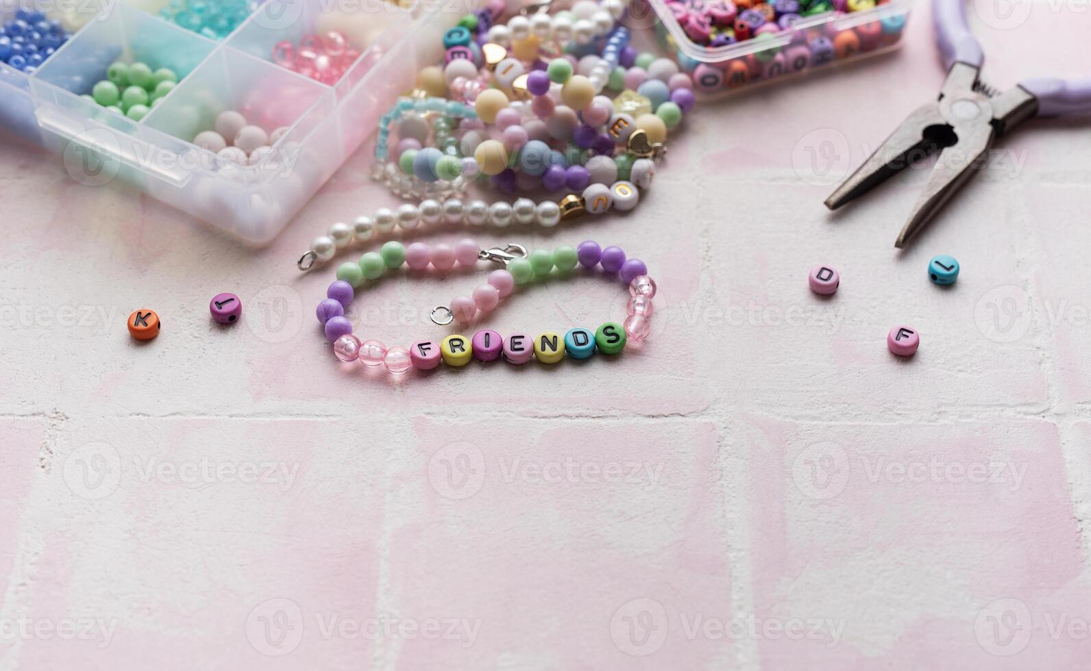Colorful beads and pliers arranged on pink tile for jewelry making photo