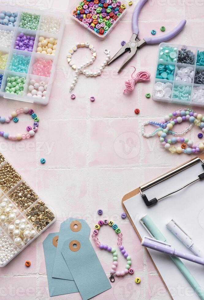 Colorful beads and jewelry making supplies arranged on pink tile background with clipboard and pens photo