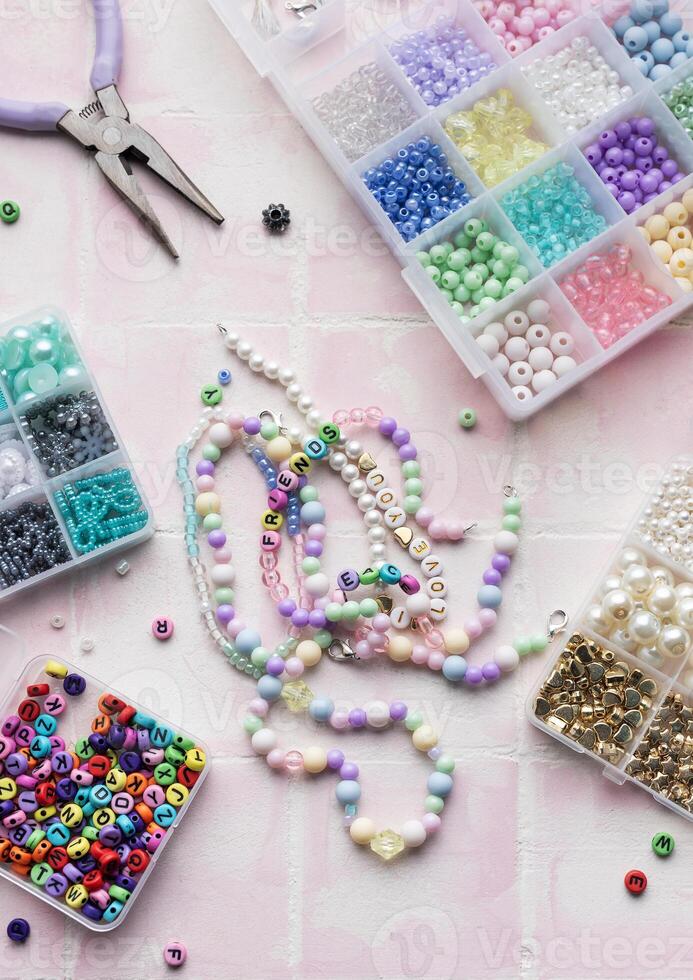 Colorful beads and jewelry making tools arranged on pink tile surface photo