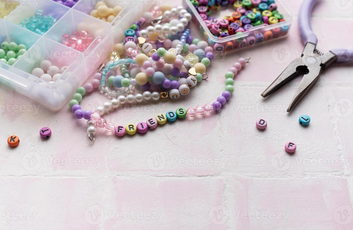 Colorful beads and pliers arranged on pink tile for jewelry making photo