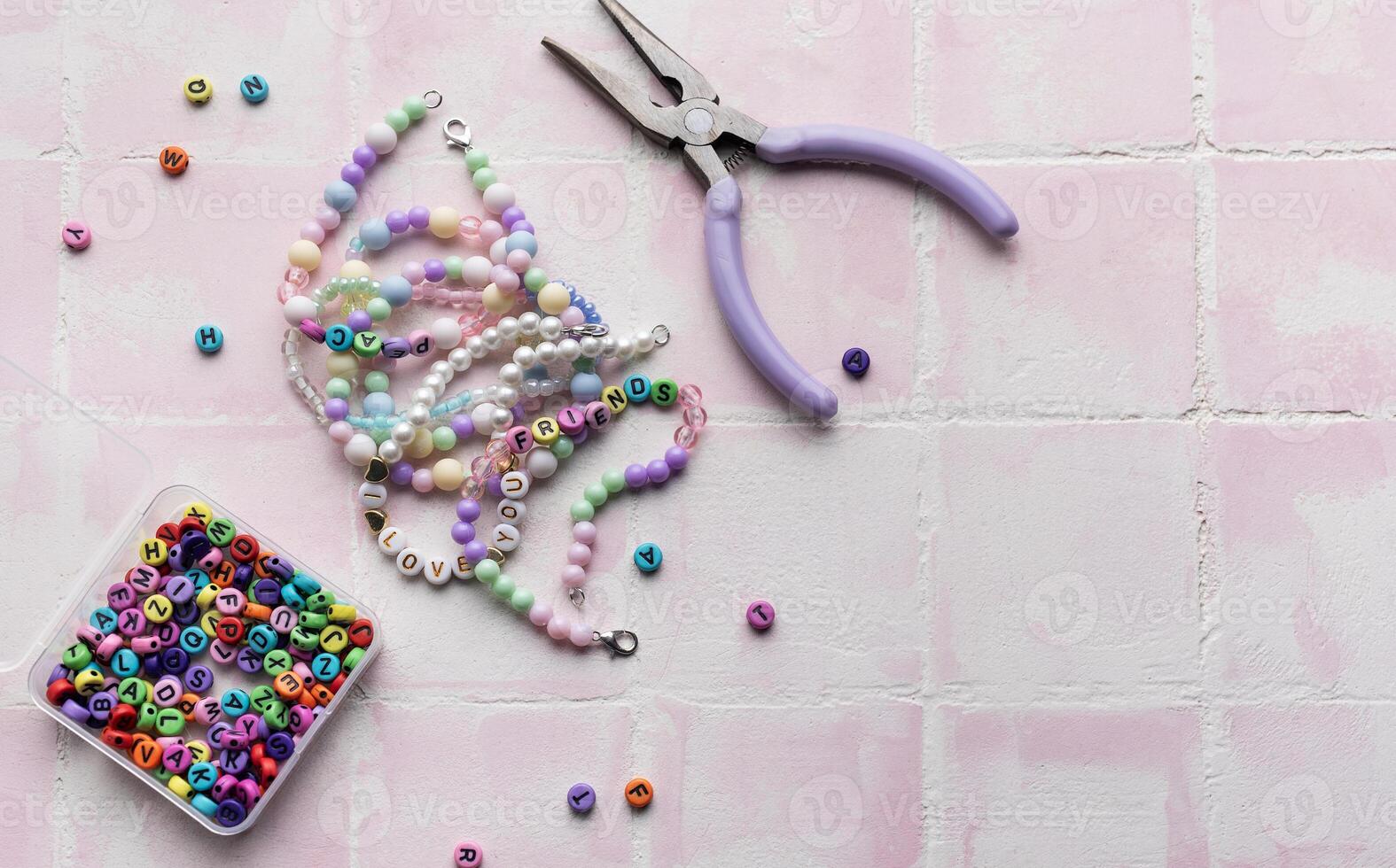 Colorful beads and jewelry making tools arranged on pink tile surface photo