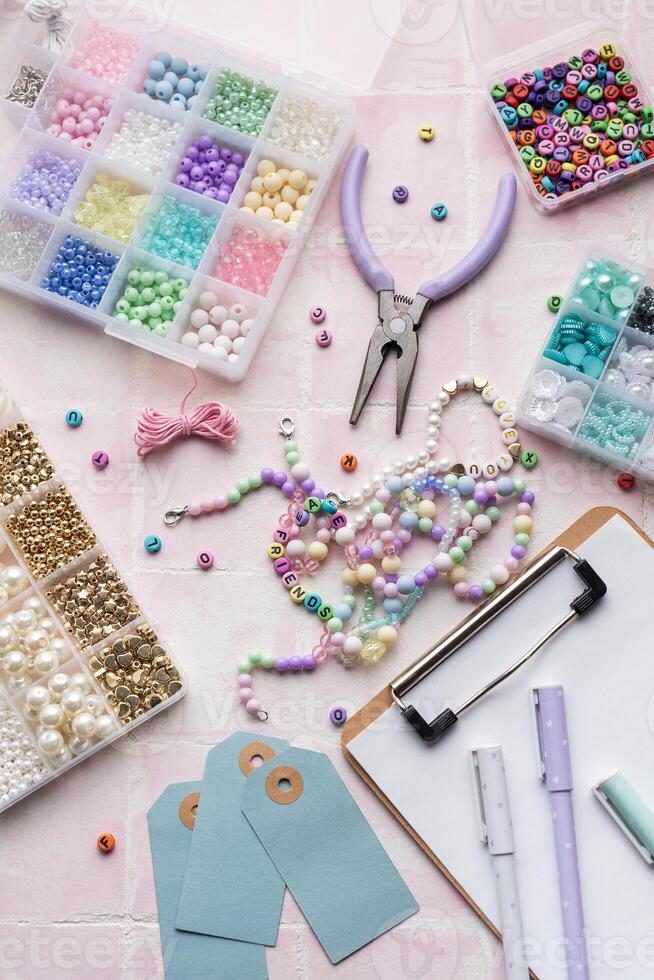 Colorful beads and jewelry making supplies arranged on pink tile background with clipboard and pens photo