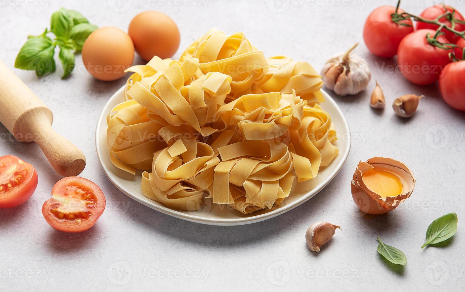 Uncooked pappardelle pasta with ingredients forming frame on table photo