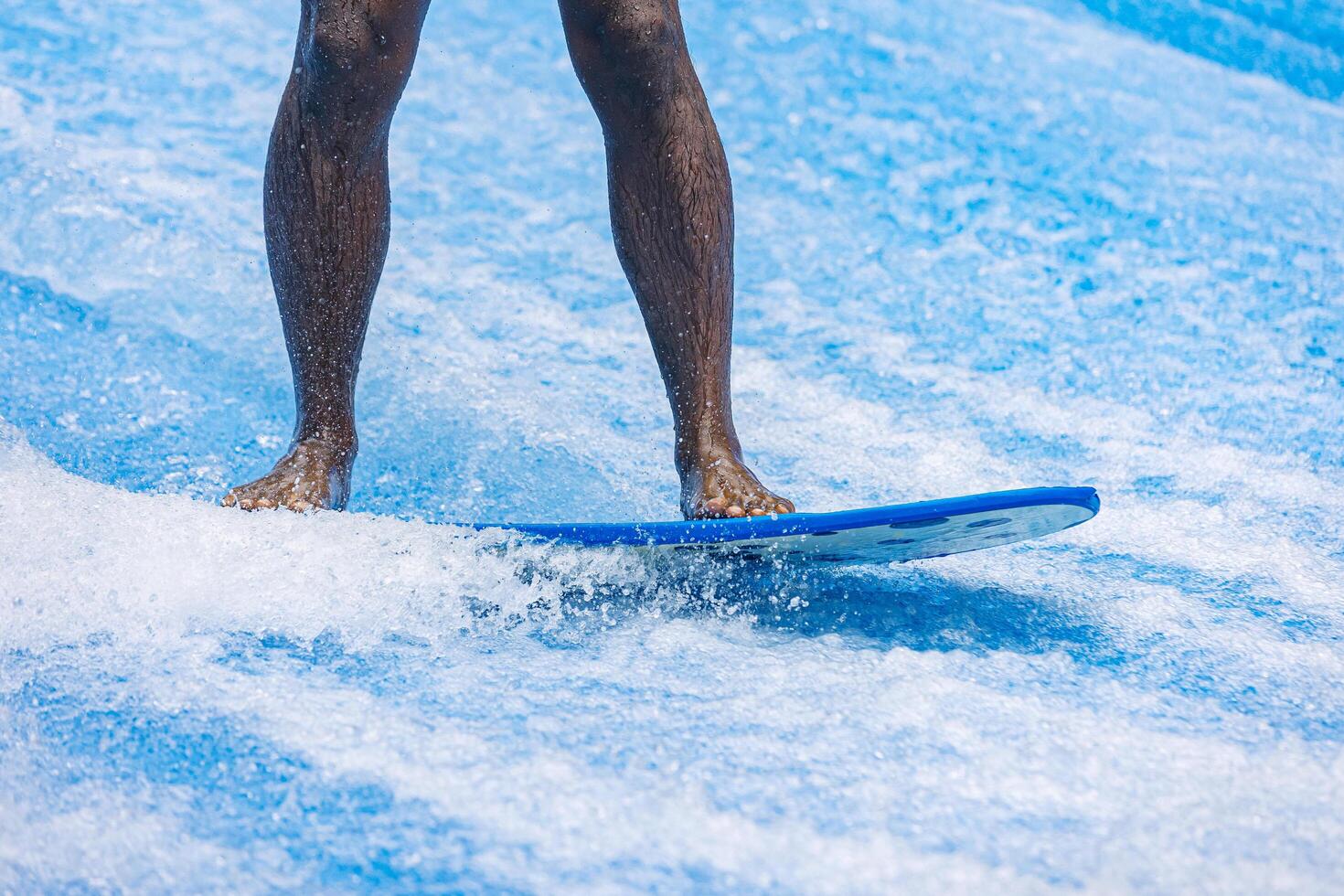 Black man rides a surfboard on a wave simulator indoors. Young surfer during training on generated waves. Water sports and recreation. photo