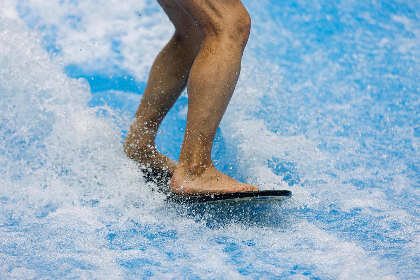 Man legs rides a surfboard on a wave simulator indoors. Young surfer during training on generated waves. Water sports and recreation. photo