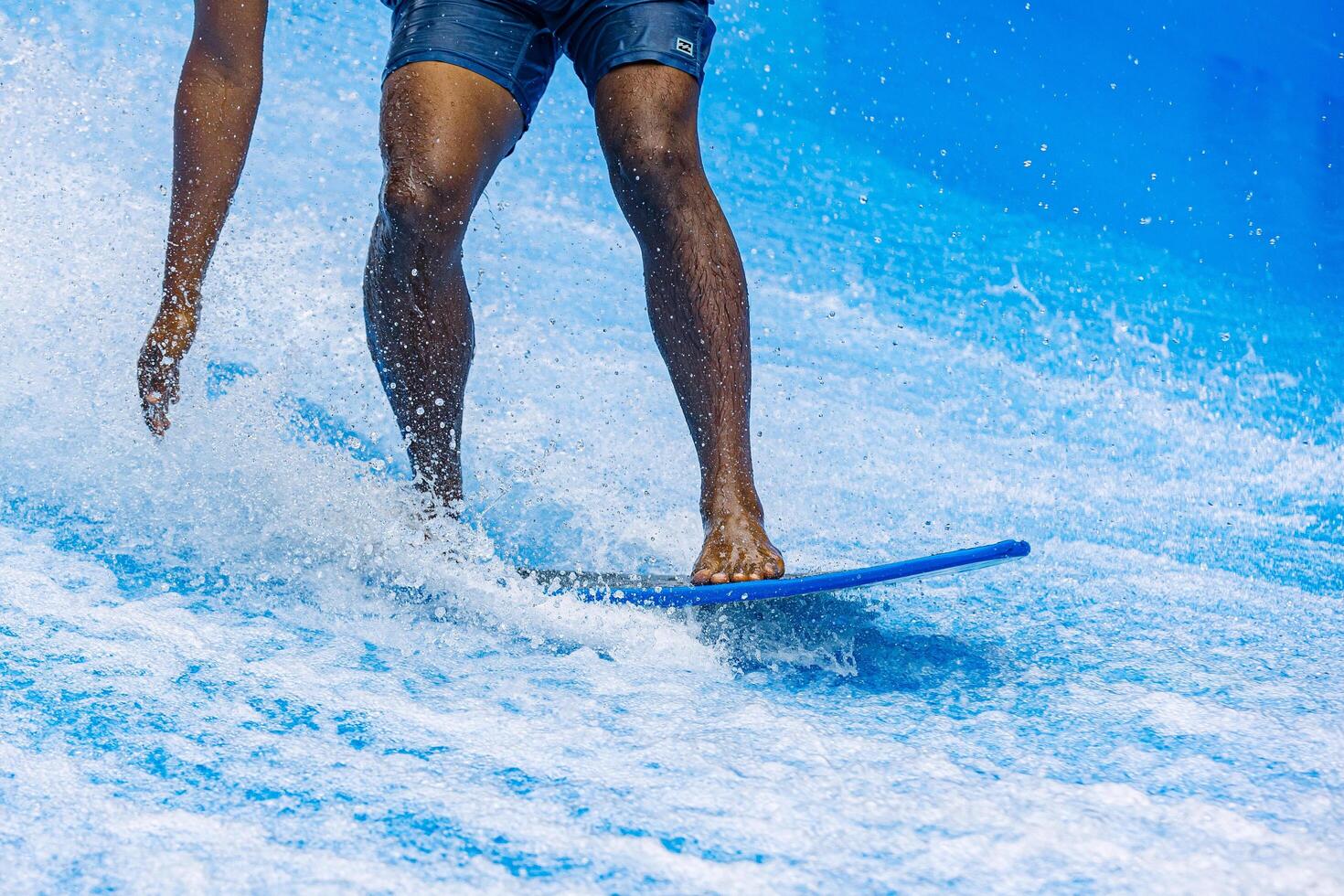 Black man rides a surfboard on a wave simulator indoors. Young surfer during training on generated waves. Water sports and recreation. photo