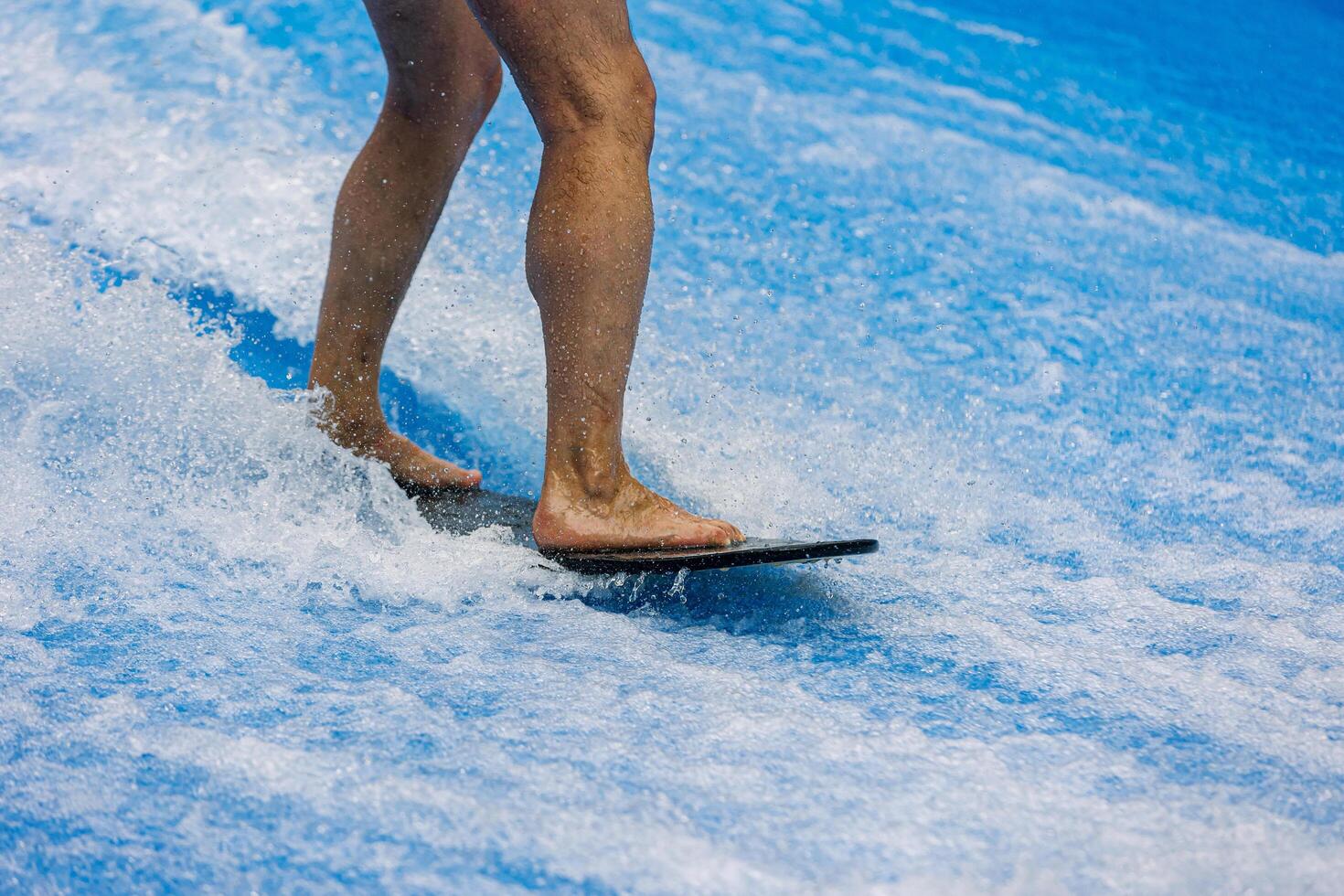 Man legs rides a surfboard on a wave simulator indoors. Young surfer during training on generated waves. Water sports and recreation. photo