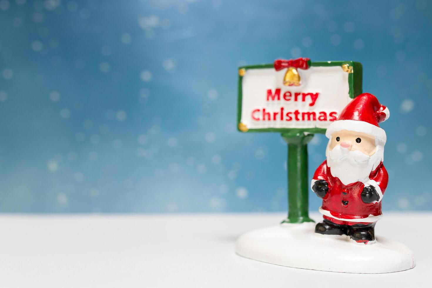 Miniature Santa Claus figurine standing next to a festive Merry Christmas sign photo