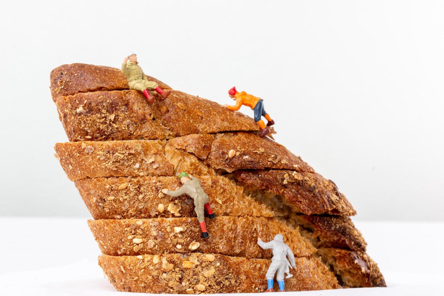 Miniature figurines climbing a stack of multigrain bread slices, resembling a rugged mountain photo