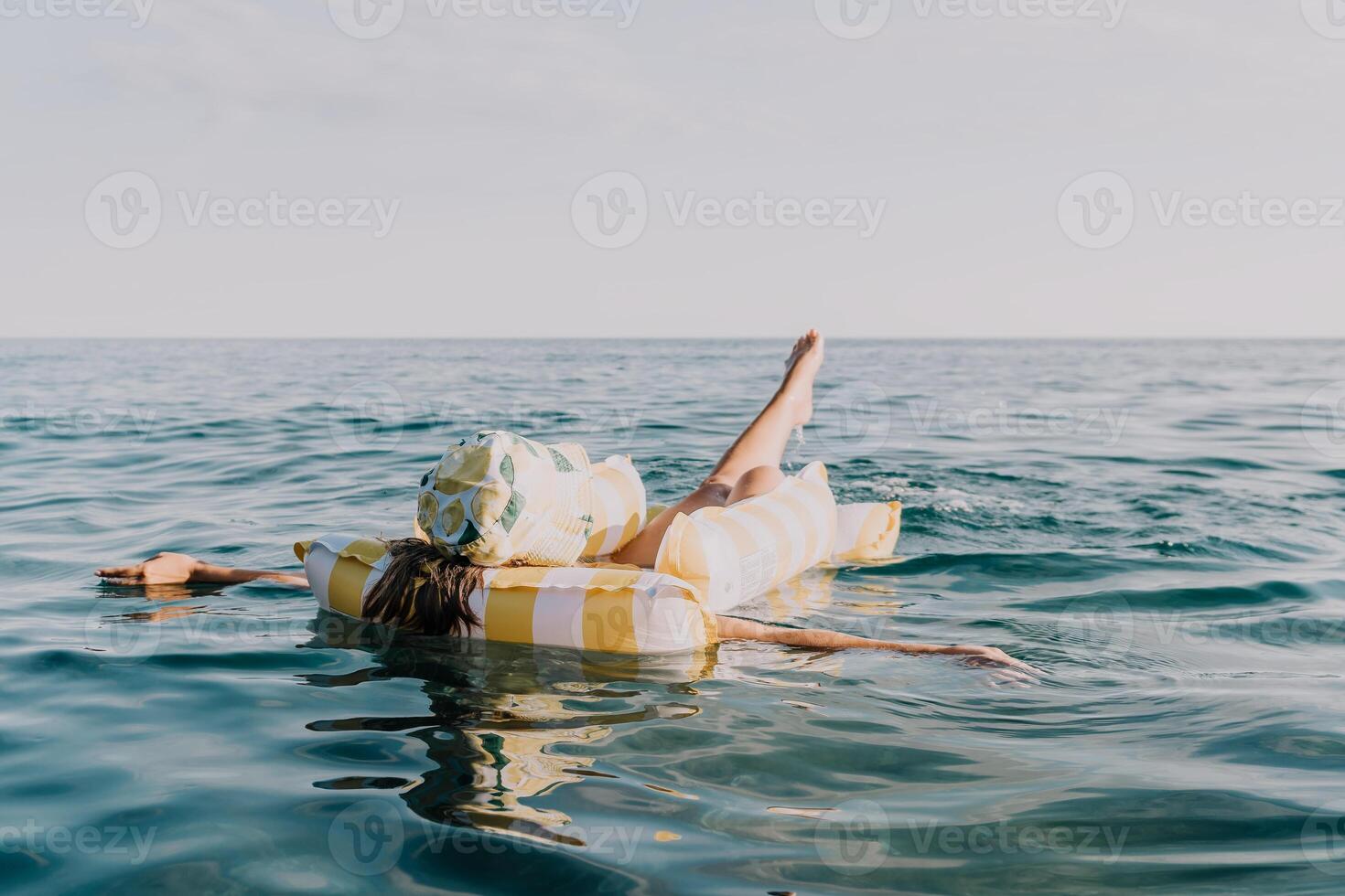 Woman Inflatable Raft Ocean Relaxing - A woman reclines on a striped inflatable raft, floating on the ocean's surface. The vastness of the water and the peaceful scene suggest relaxation and enjoyment photo