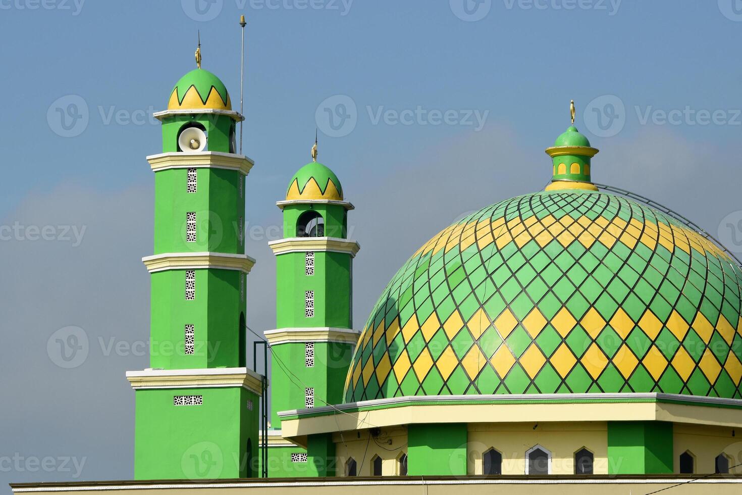 Beautiful mosque dome and two minarets with green and yellow theme against clear blue sky background photo