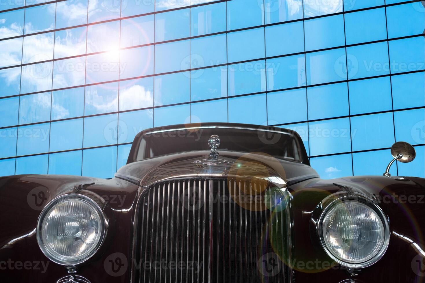 Vintage, black, shiny car on a background of a mirrored wall of a modern building. photo