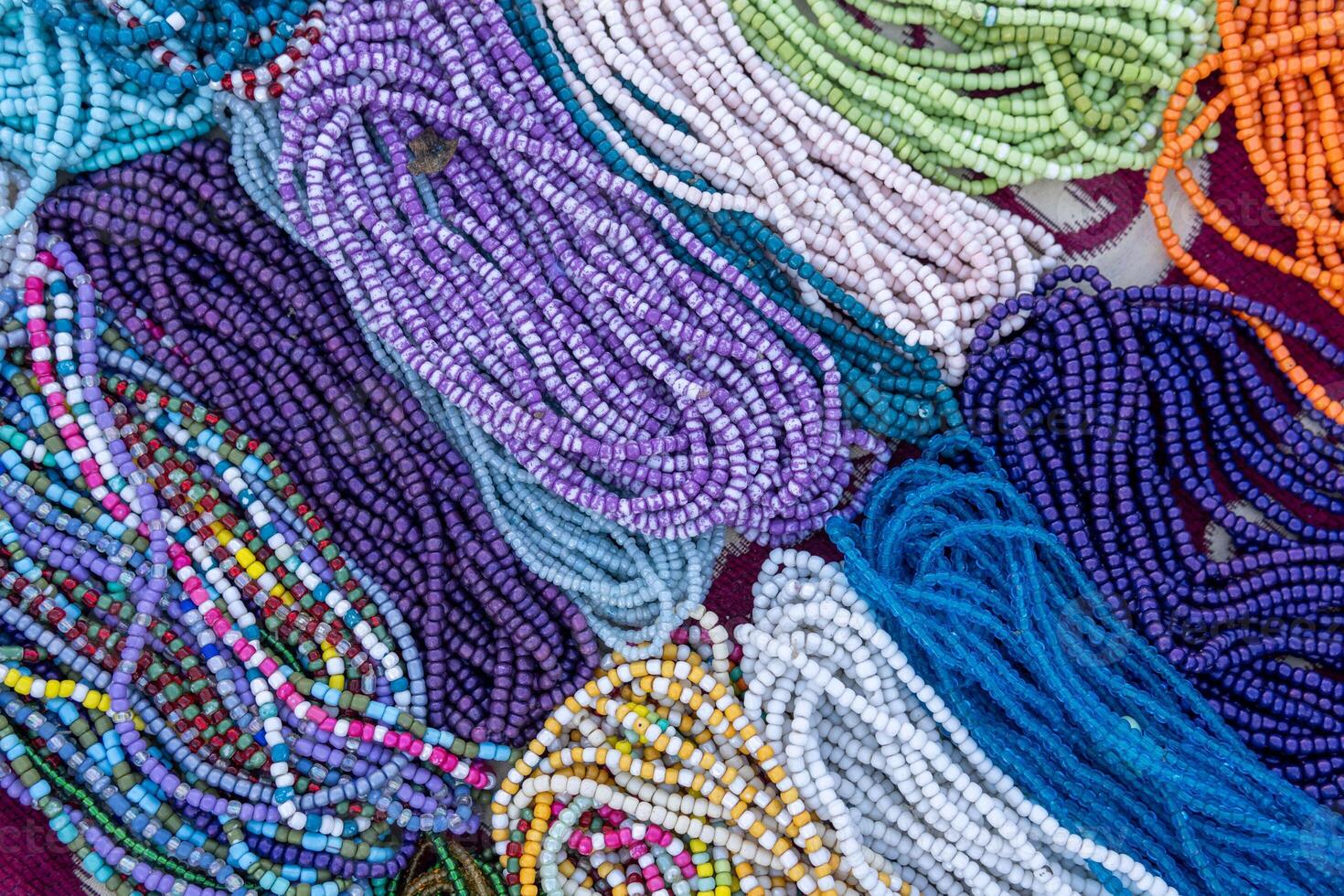 A variety of colorful beaded necklaces and bracelets laid out on a surface. Some beads are round and smooth, while others are irregularly shaped. photo