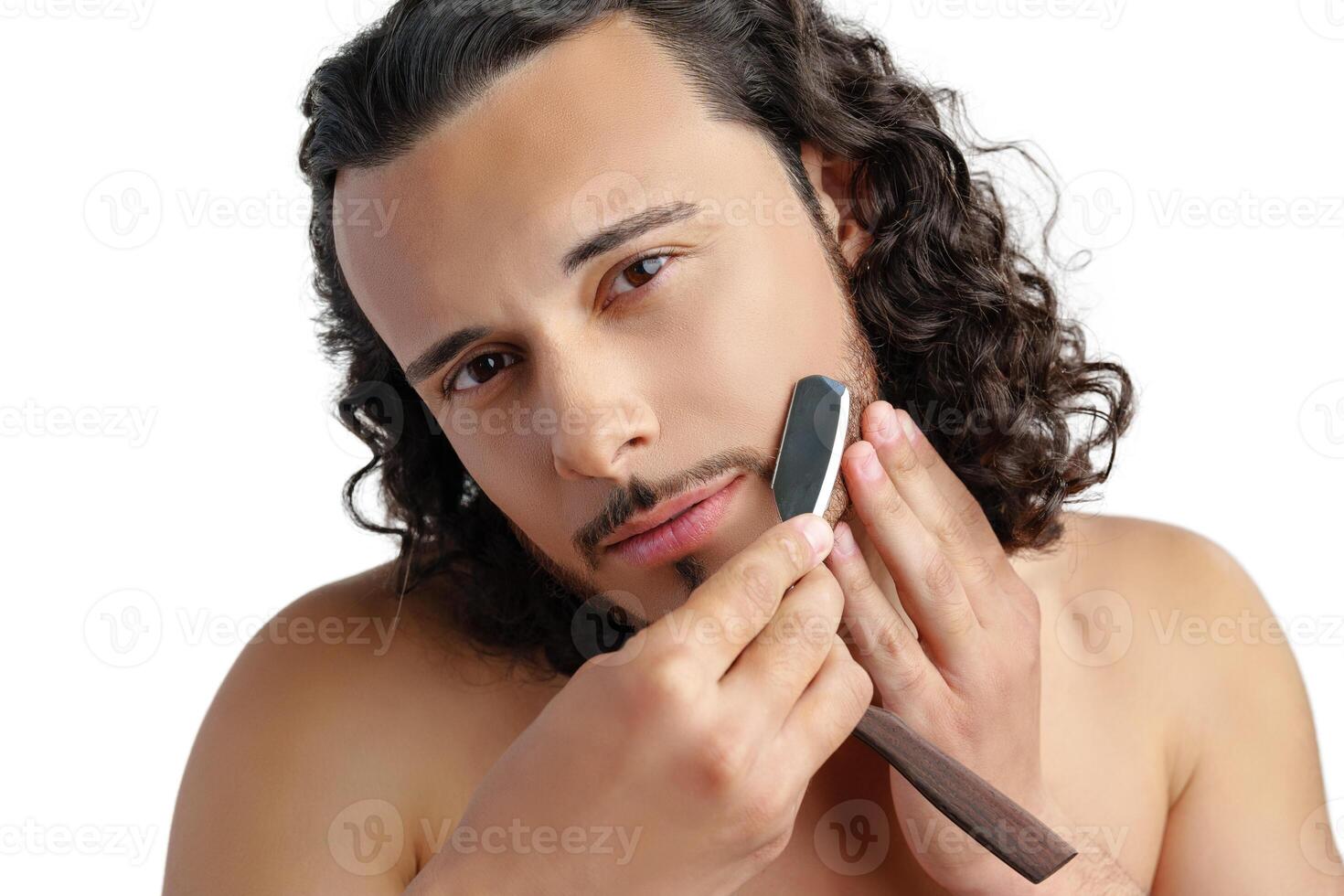 A man with curly hair grooming his beard in a well-lit space while using a straight razor photo