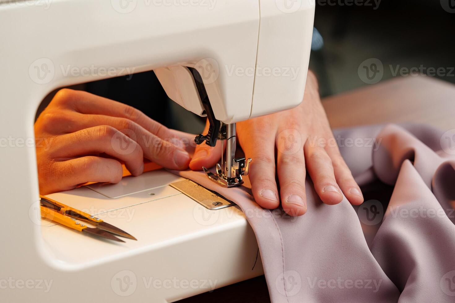 Hands sewing fabric using a sewing machine on a wooden table in a well-lit workspace photo